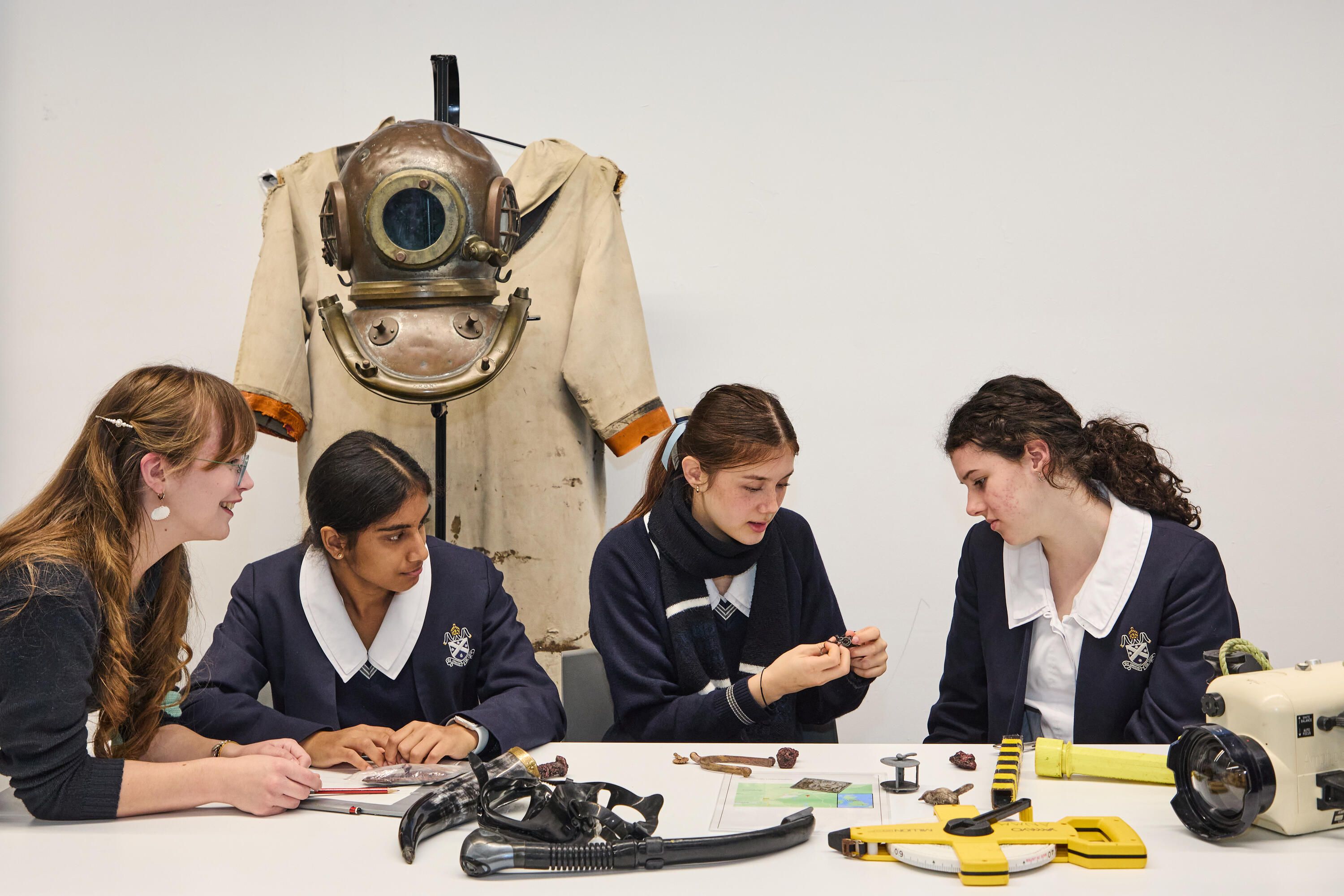 Photo of 3 female high school students sitting at a table looking at objects
