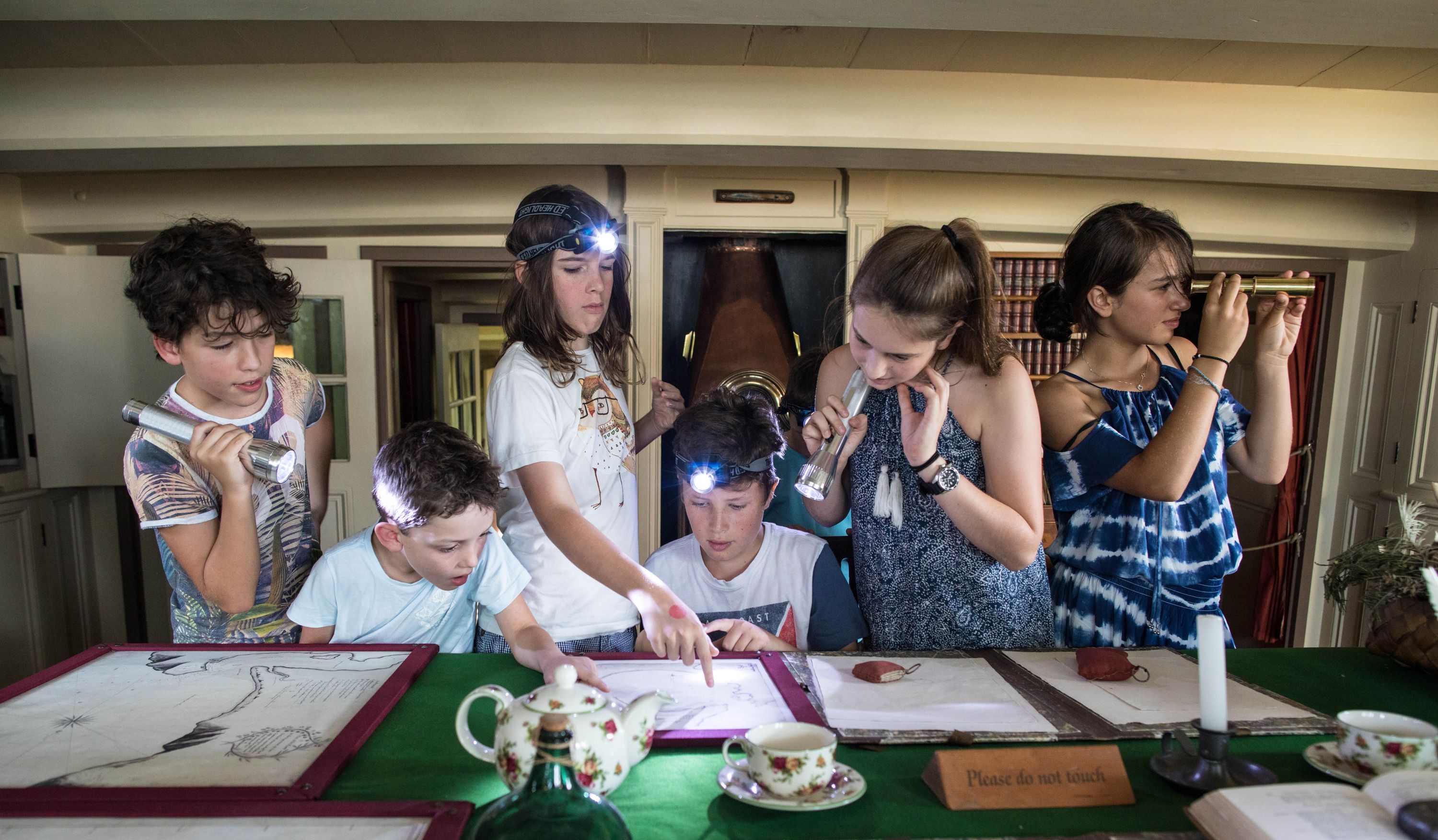Group of children of different ages, with torches, looking at documents on a table