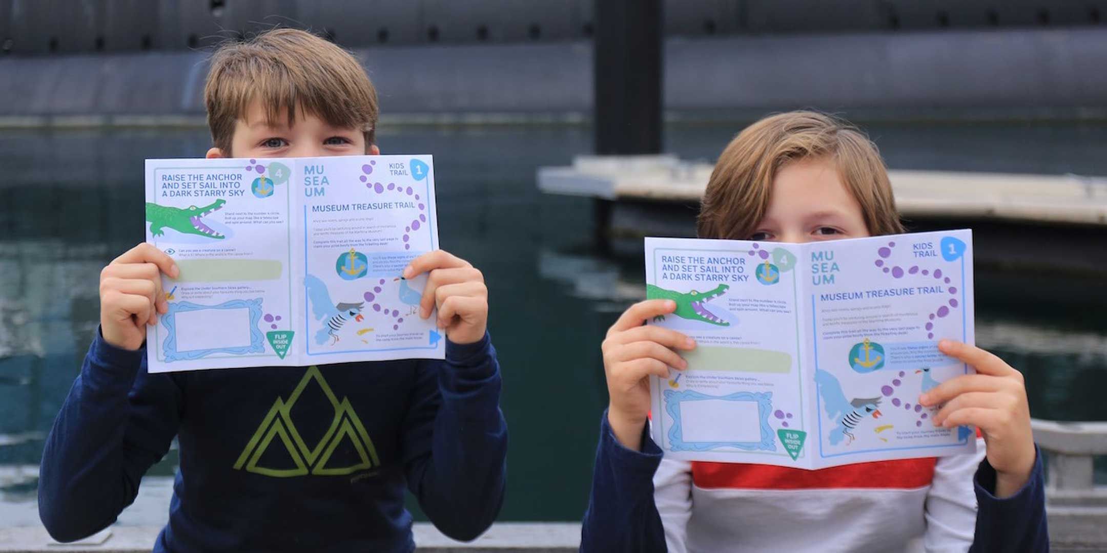 Photo showing 2 boys holding an activity booklet up, obscuring the bottom half of their faces.