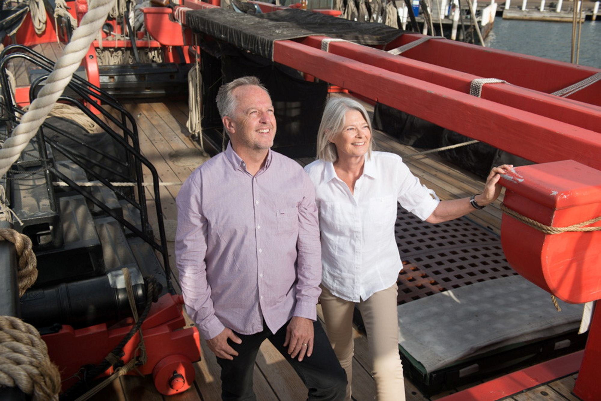 Photo showing an older couple walking around a wooden tall ship. 