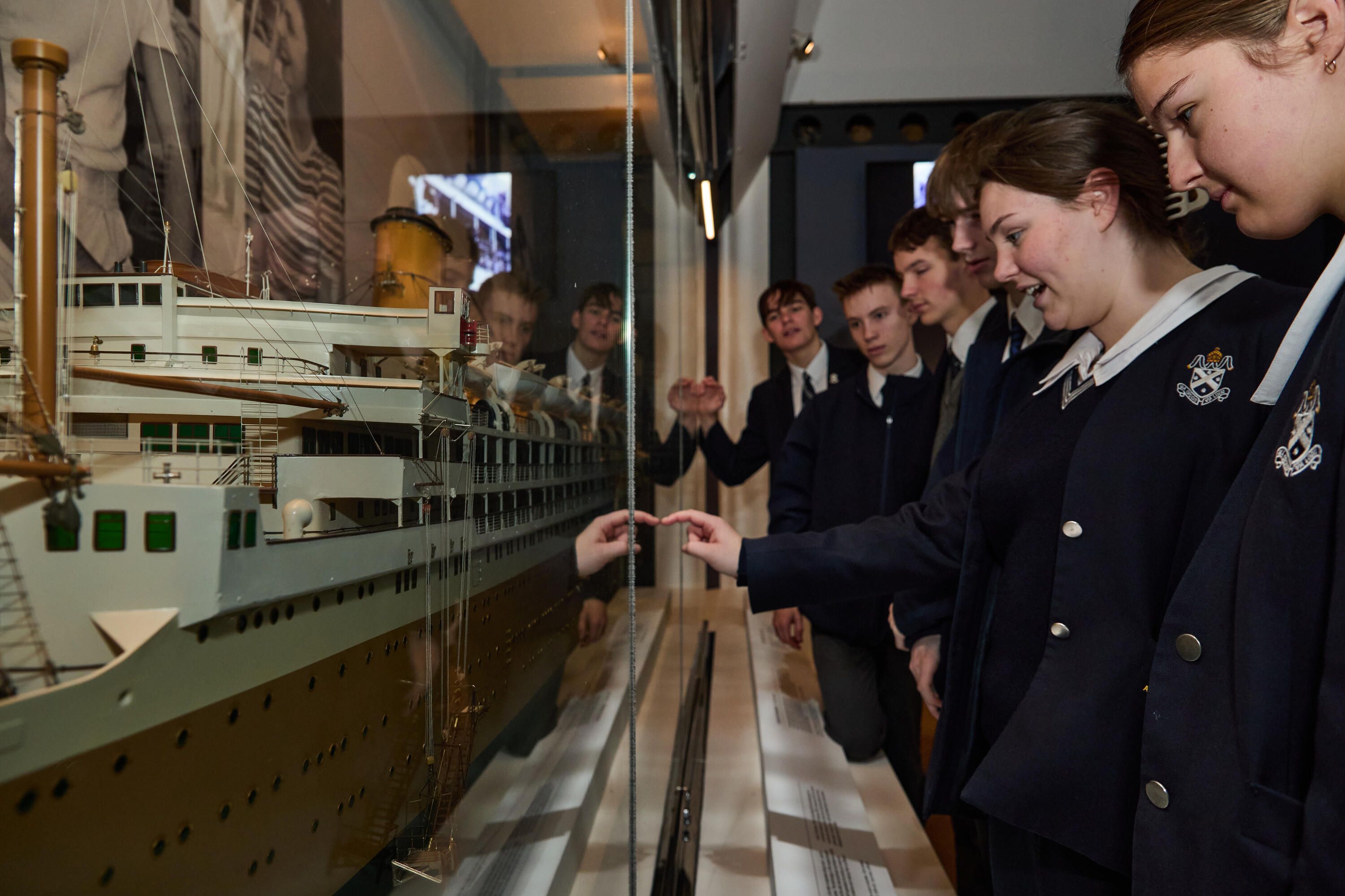 image of a model of an ocean liner in a display case, with a line of high school students looking at it.