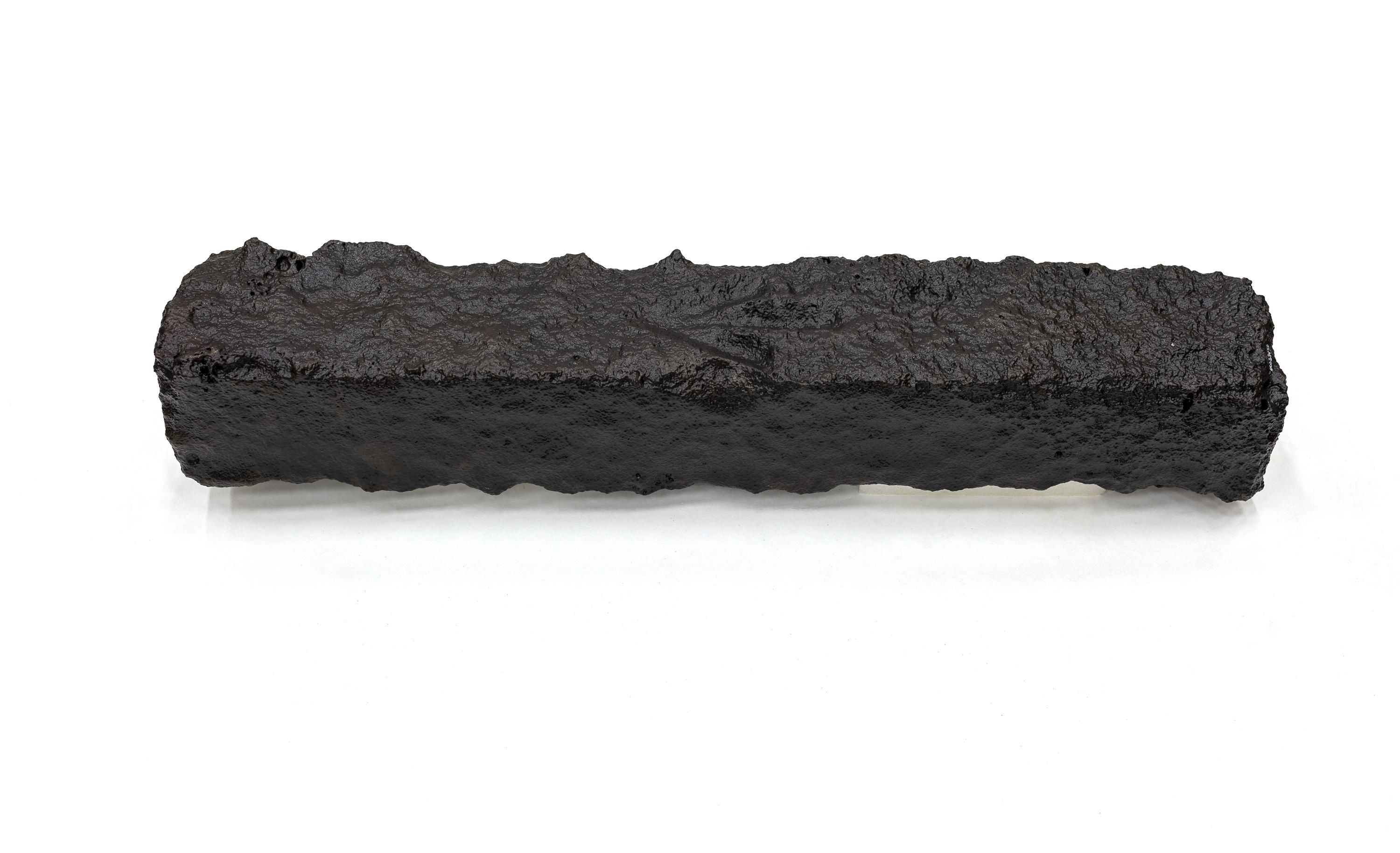 A photo of a rectangular piece of rough, black metal. 