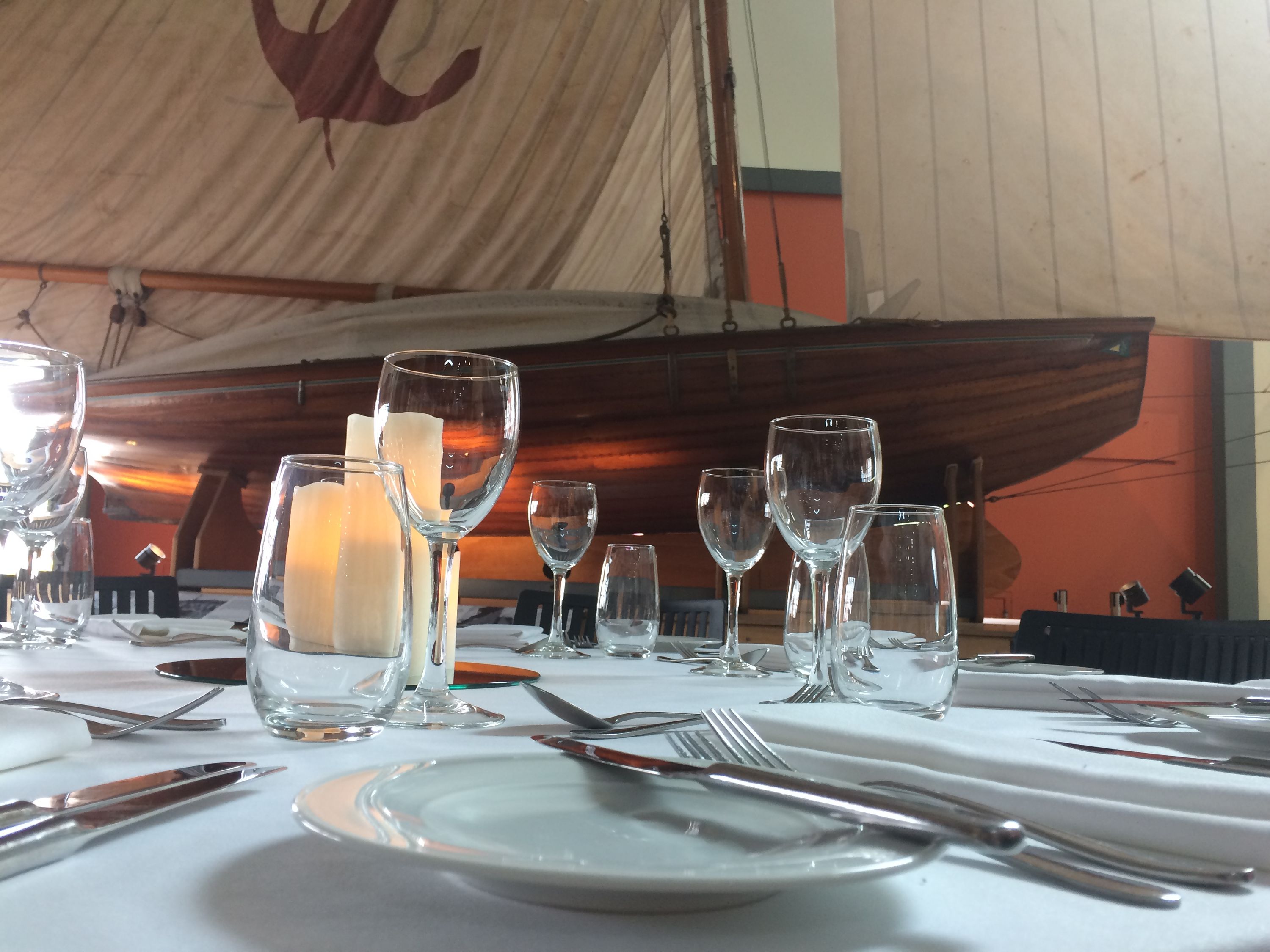 close up photo of a table setting on a white table cloth, with a classic wooden sailing boat in the background.
