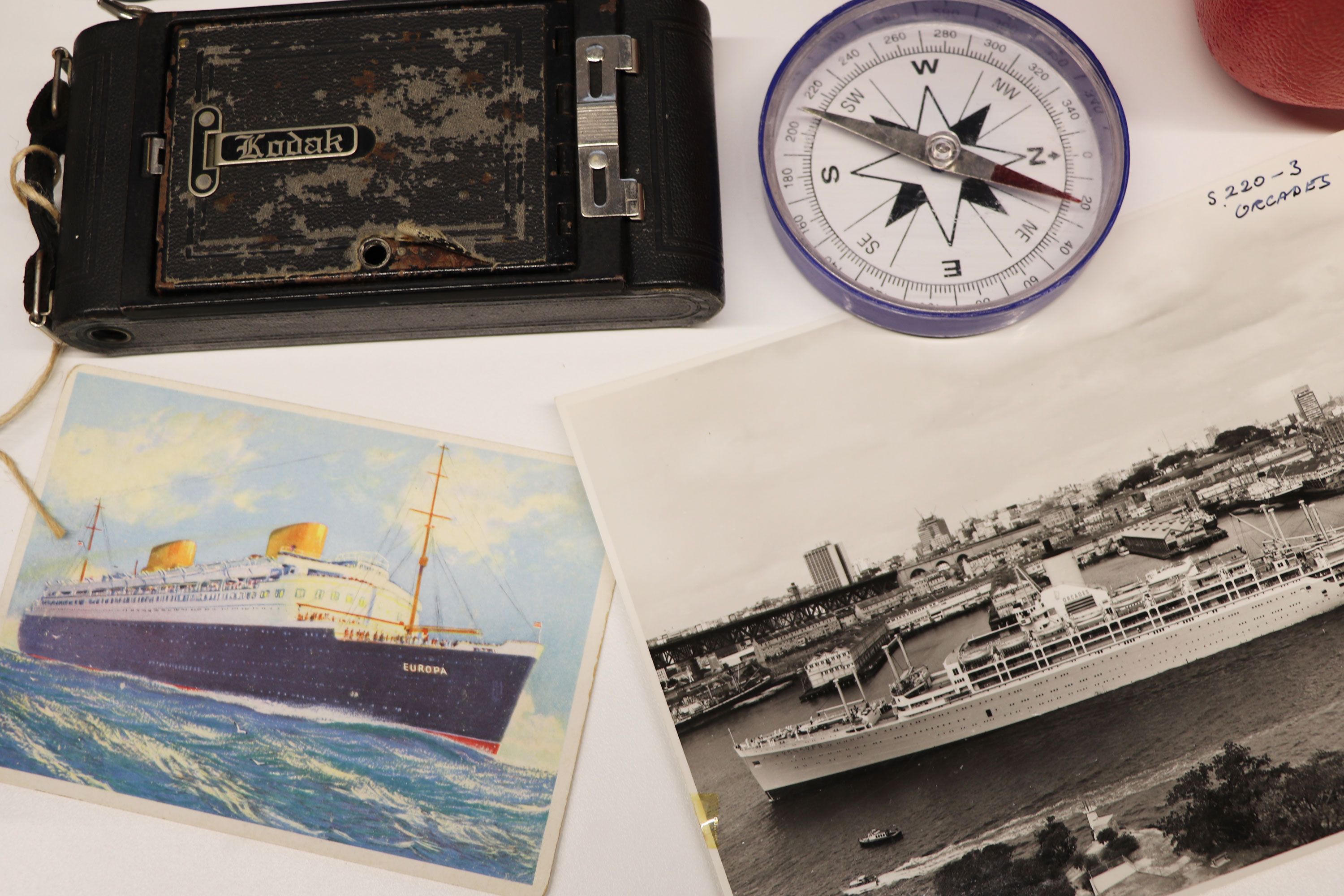 Photos and postcards, a compass and old camera on a white table.