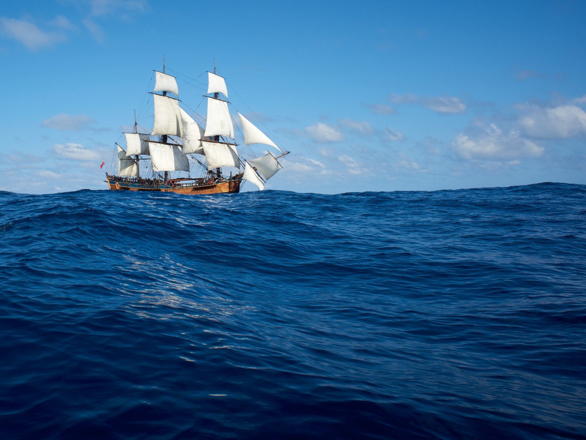 wooden tall ship with white sails on the ocean with a blue sky