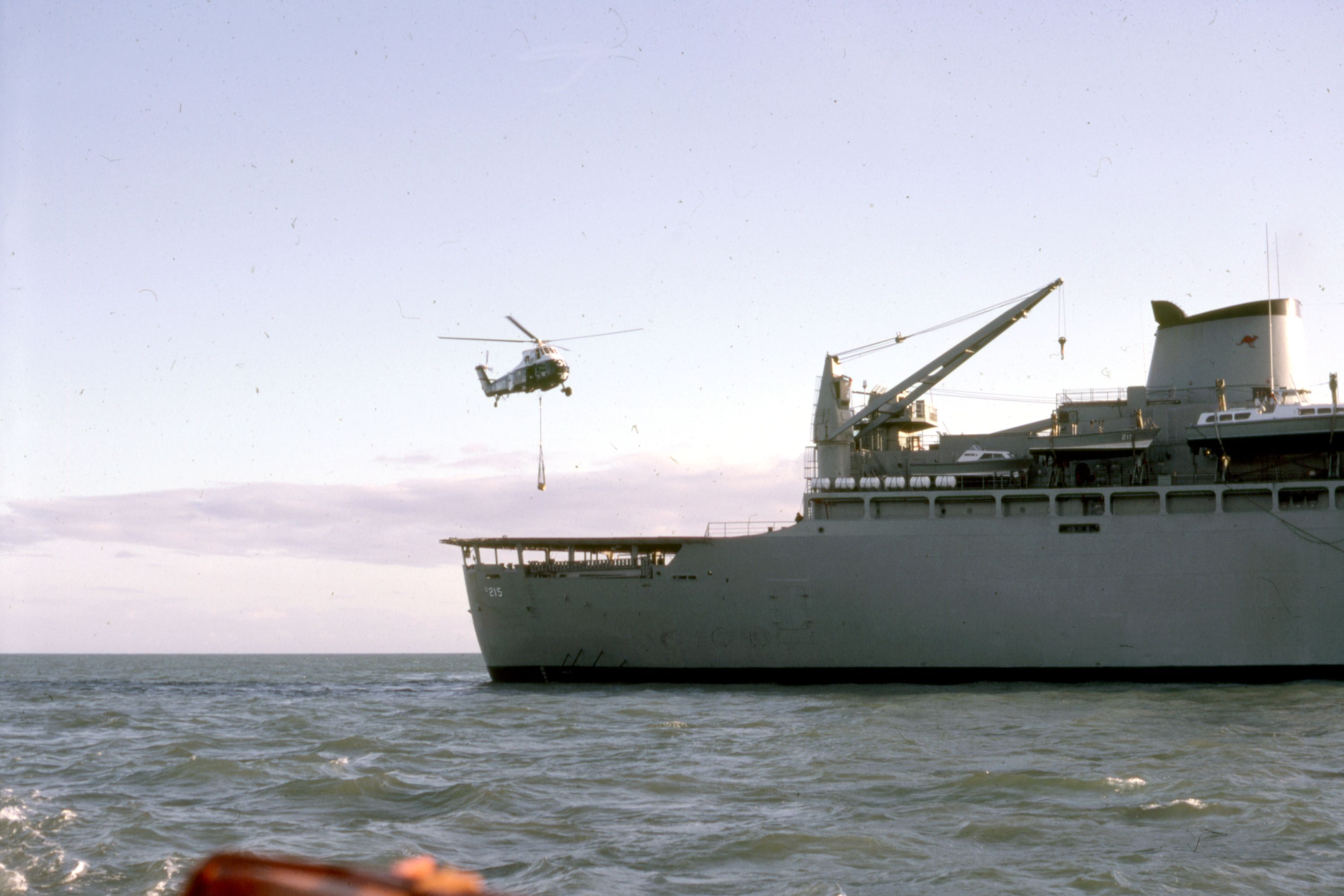 A naval ship in the distance, with a helicopter approaching. 