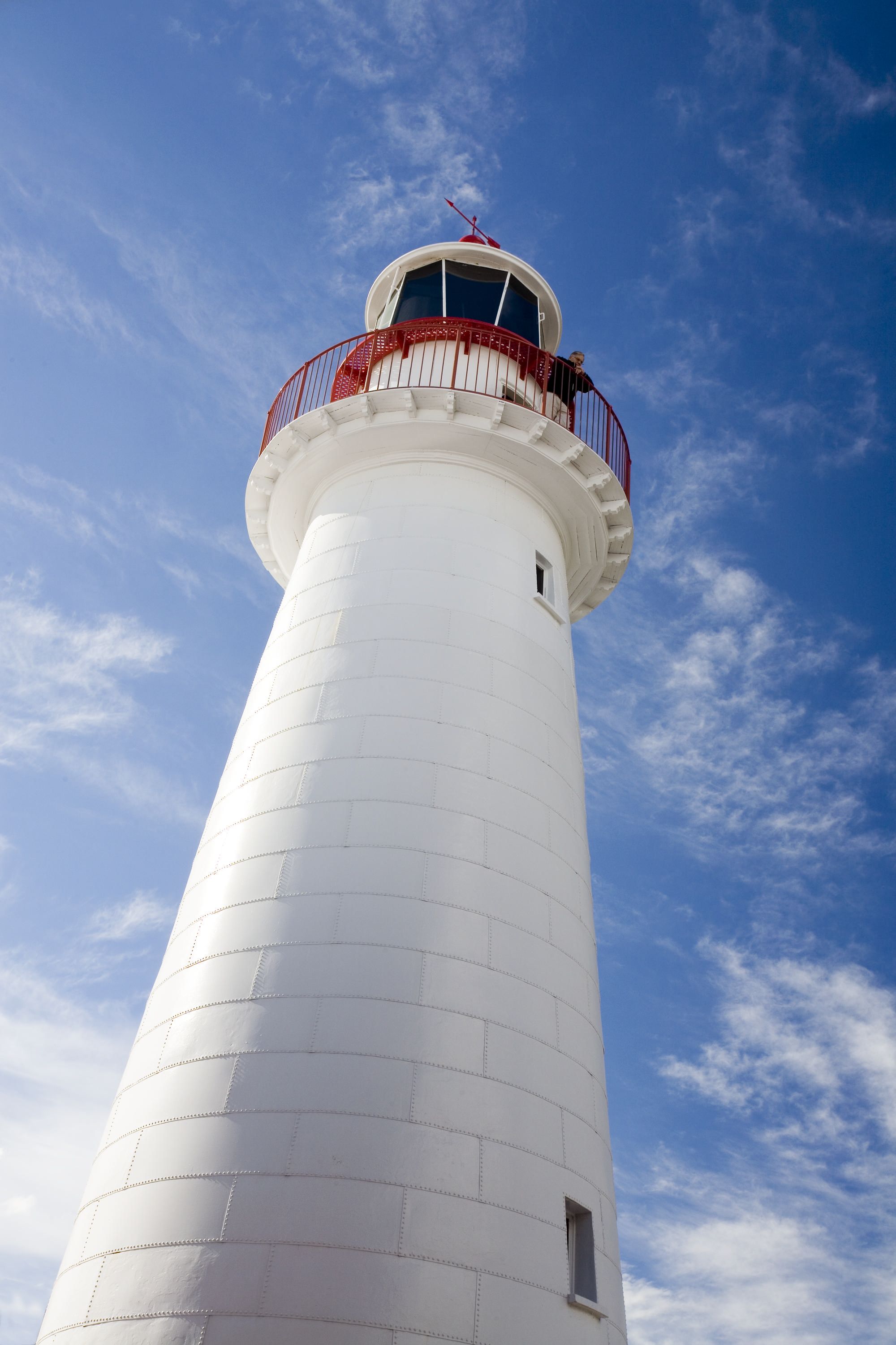 Photo of a lighthouse taken from a low angle with ablue skie and light clouds overhead.