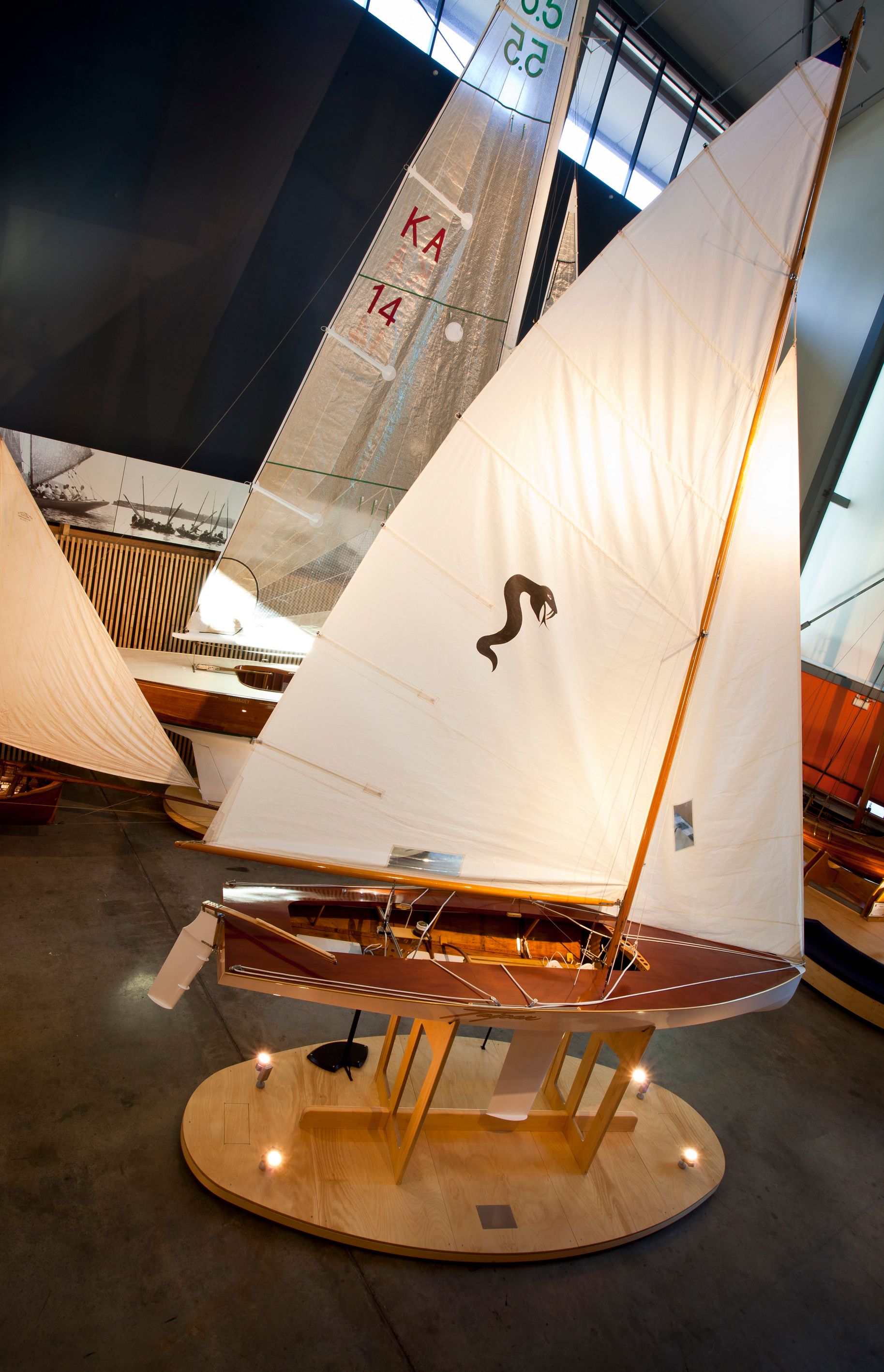 Photograph showing a wooden sailing boat with large white sails in a museum exhibition.