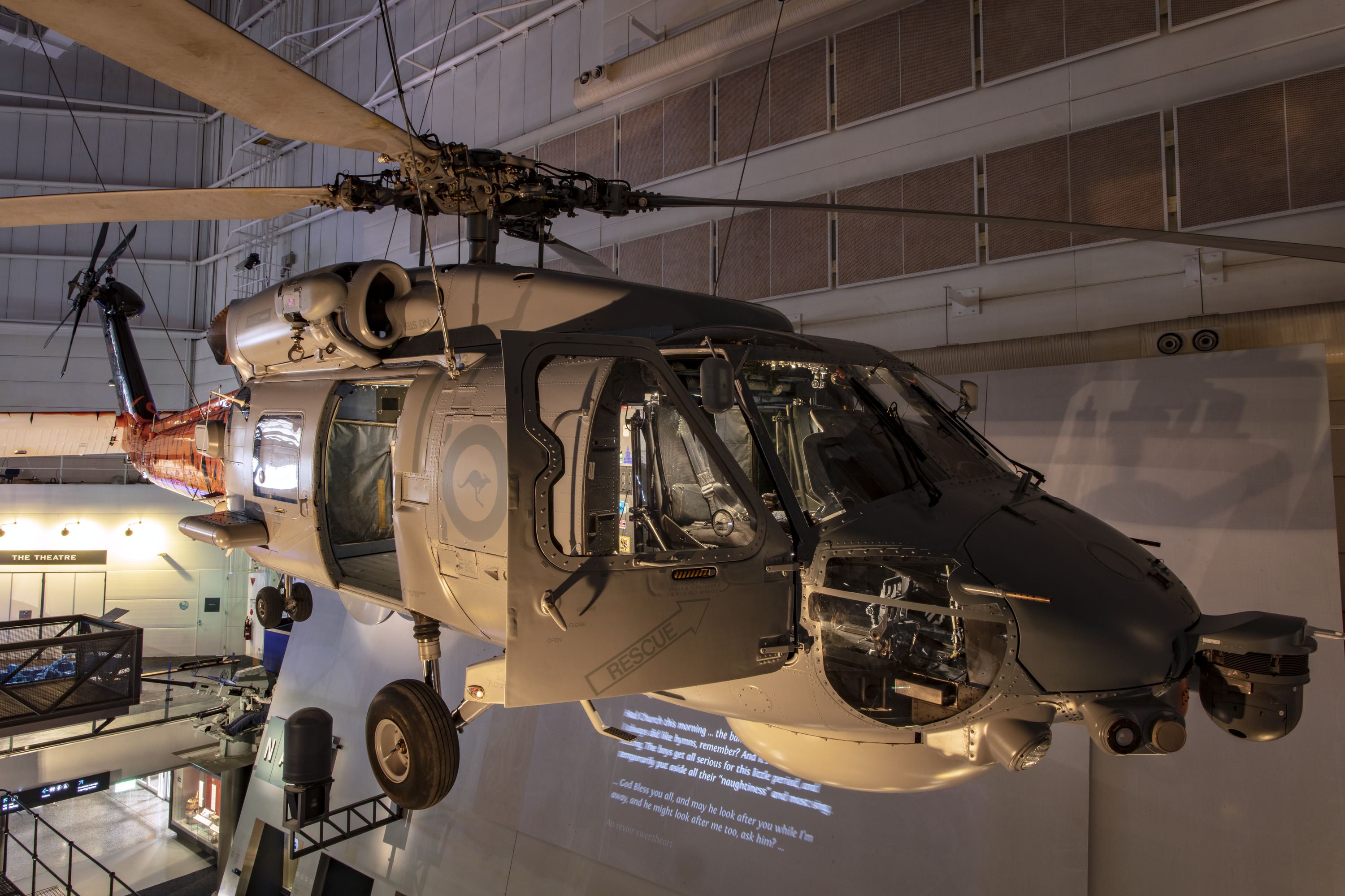 Milirary helicopter, mostly grey with orange and black tiger stripes painted on its tail, hung inside a museum gallery.  