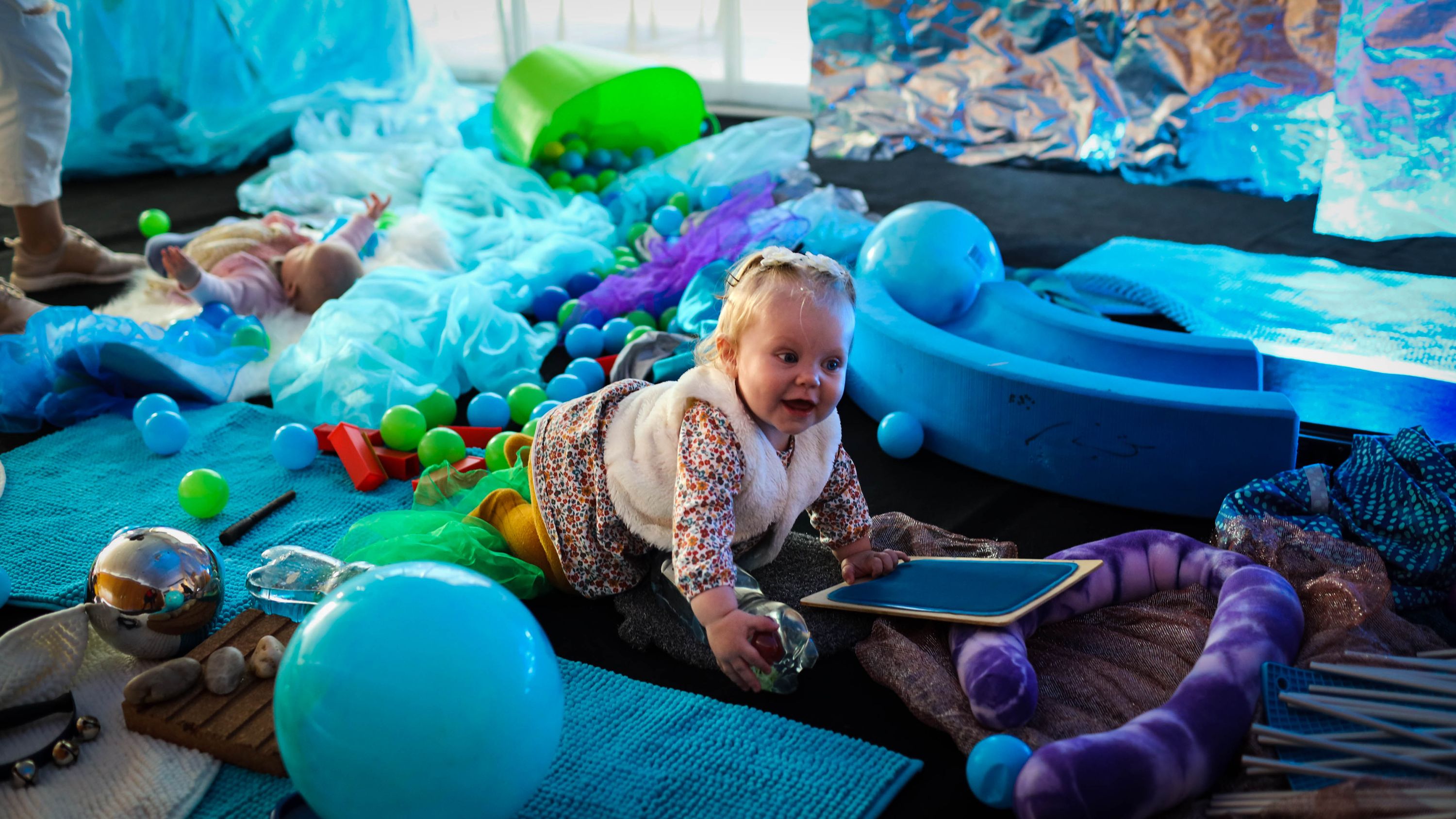 A smiling baby in the play space surrounded by toys.