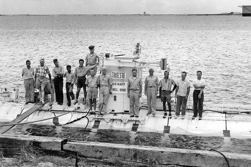 Black and white photo of a submarine on e surface of the water with 13 people standing on it.