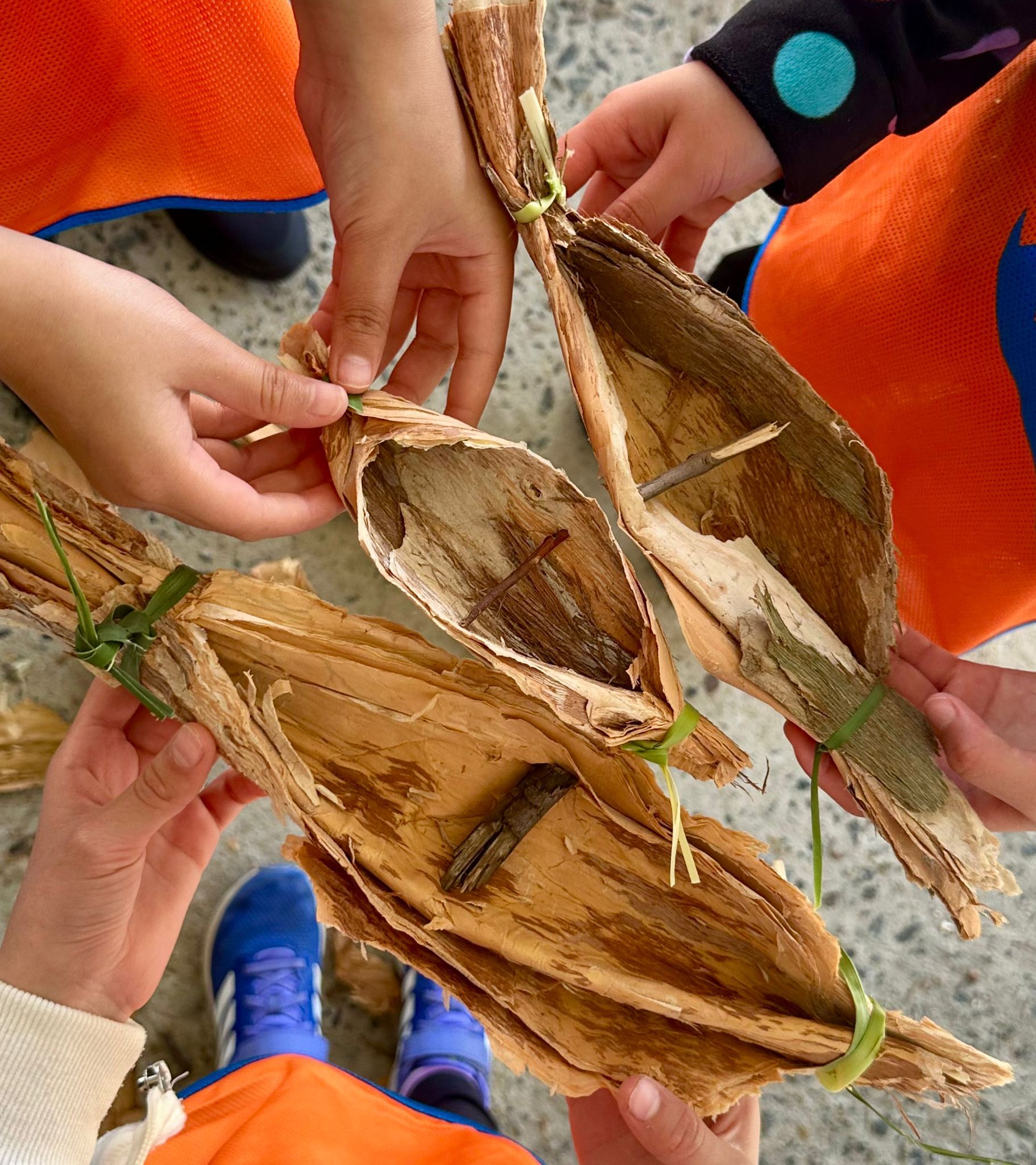Photograph showing children's hands holding small model canoes made from bark.