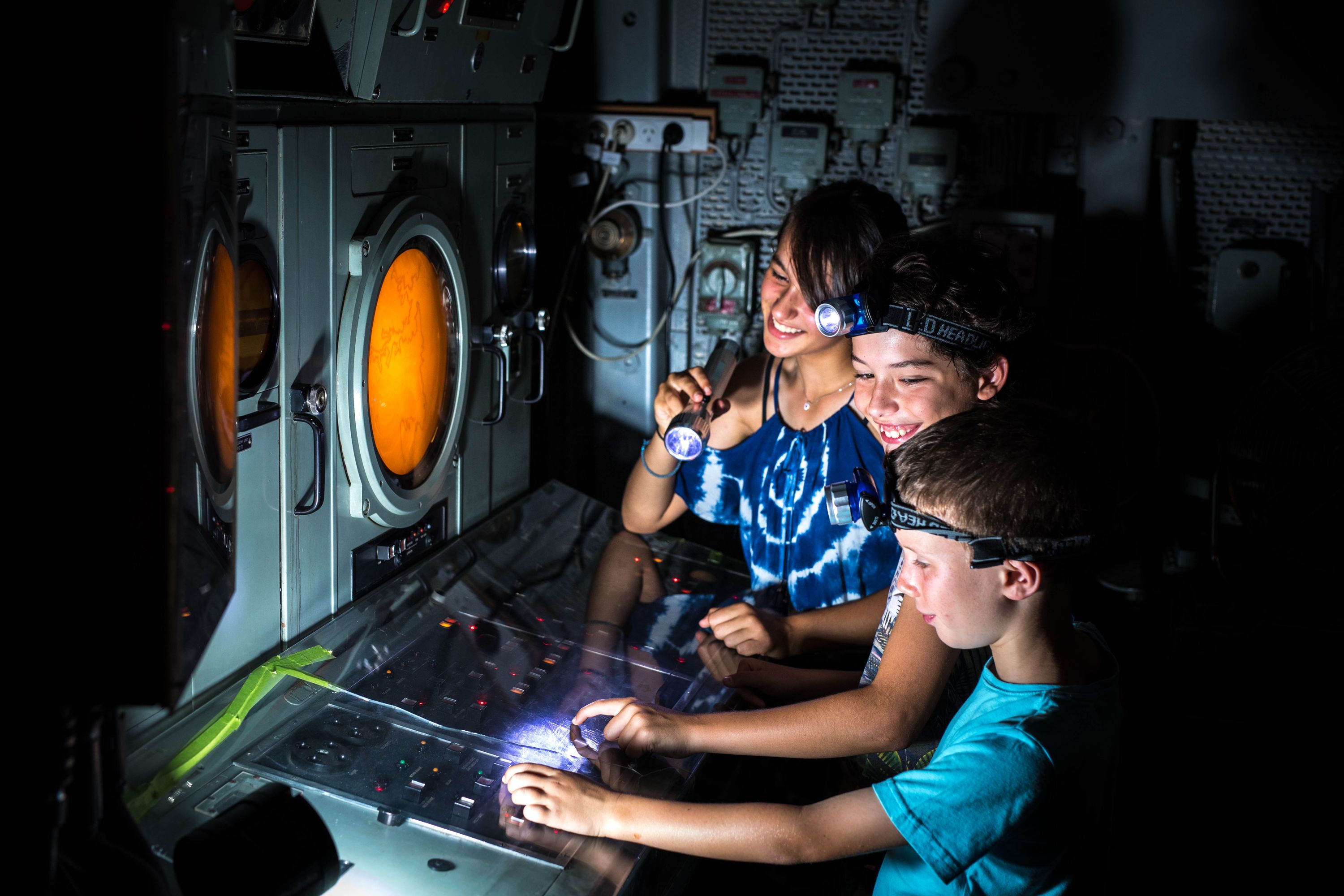 Photo of 3 children in a dark space with torches looking at a piece of technical equipment with a yellow round screen and buttons. 