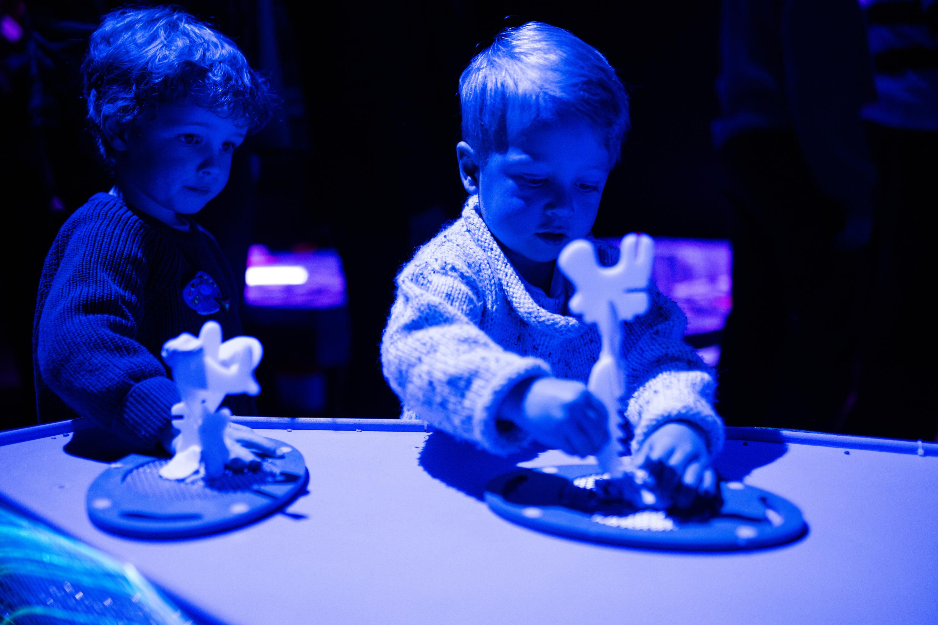 Two children in blue light playing with interactive theatre props