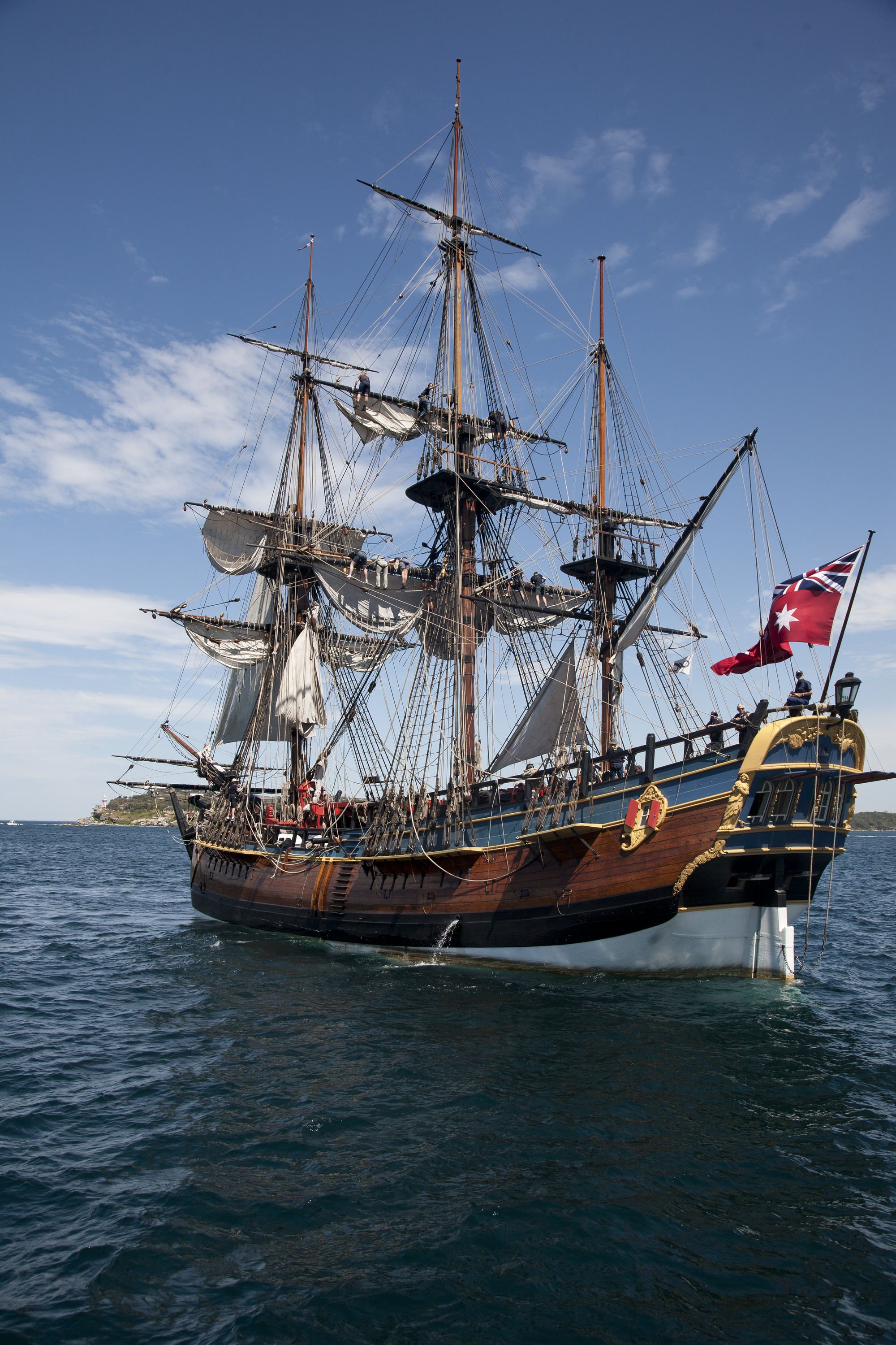 Tall ship Endeavour, photographed from behind sailing towards the left under a blue sky. 