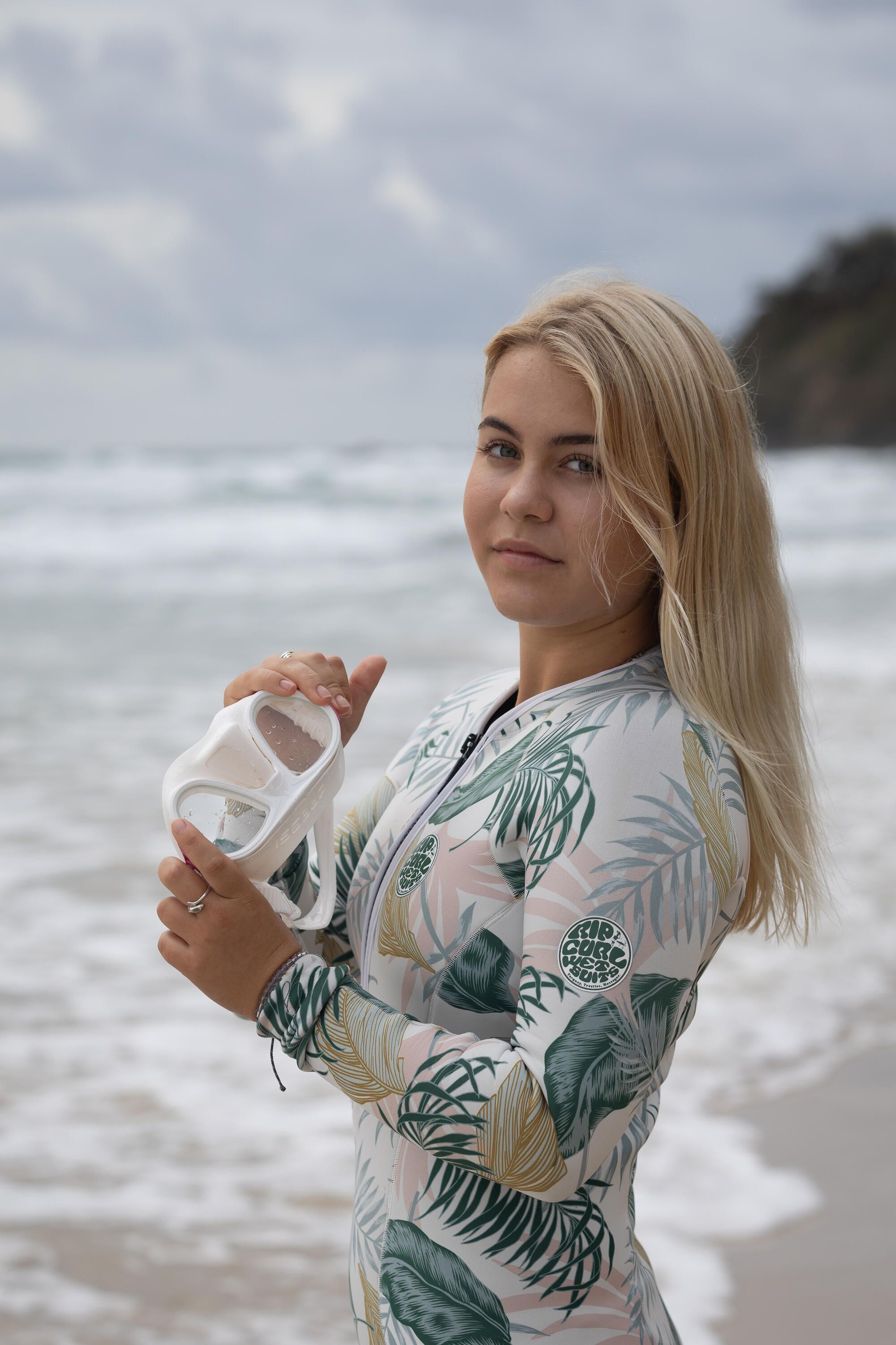 Photo of a young woman with long blond hair holding a diving mask.