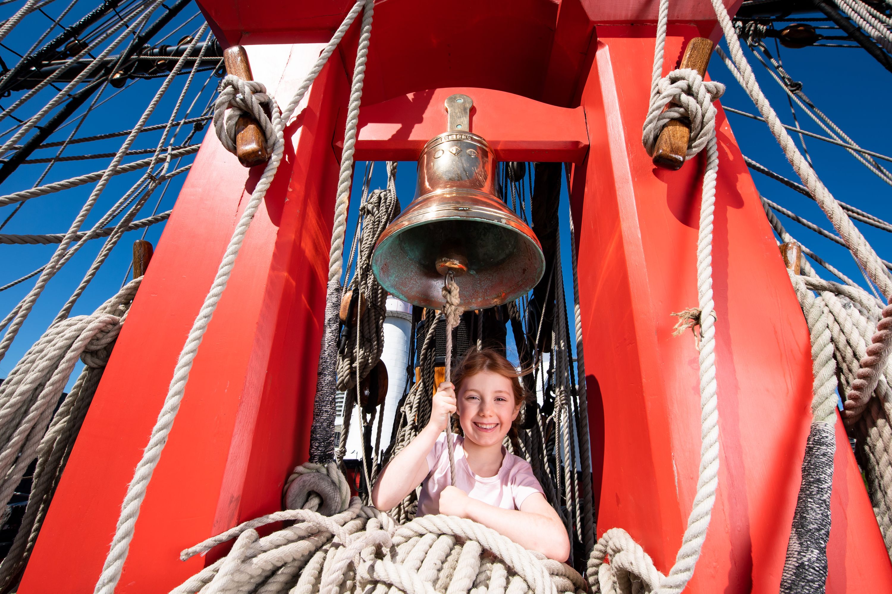 Photo of a girl ringing the ship's bell on a tall ship.