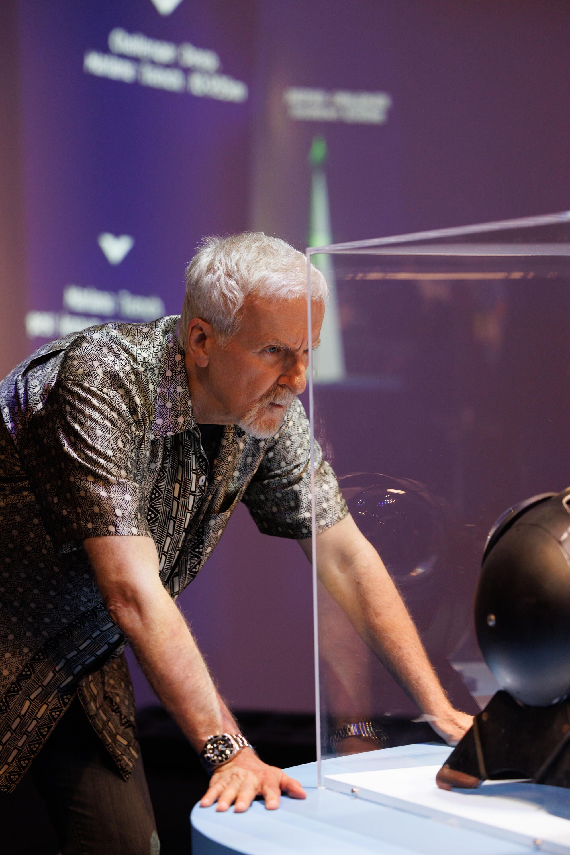 Photo of a man with grey hair and wearing a patterned shirt looking into a clear museum display case.