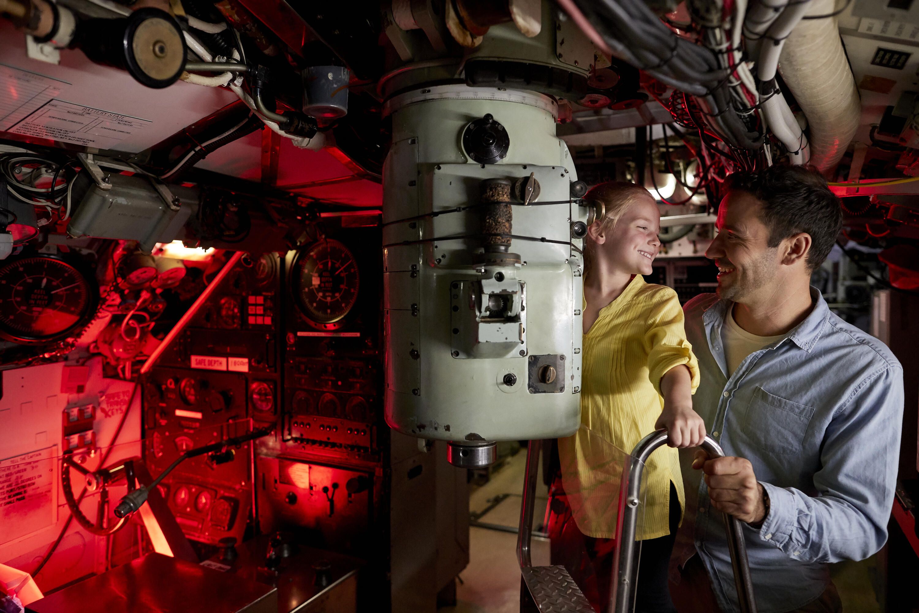 Photo of a A father and daughter looking at a periscope inside a submarine.