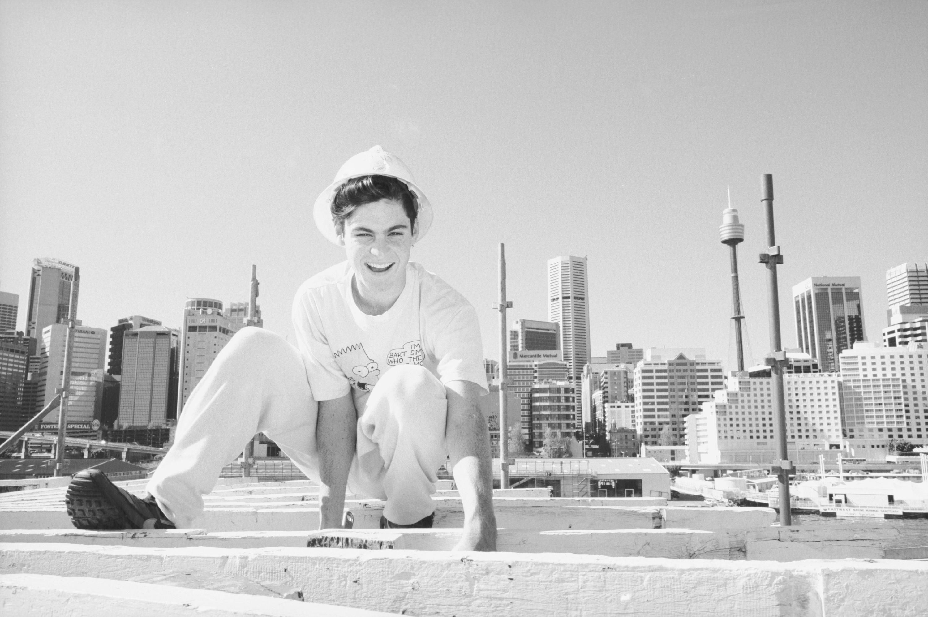 A black and white photo portrait of a young man at work with the city skyline in the background.