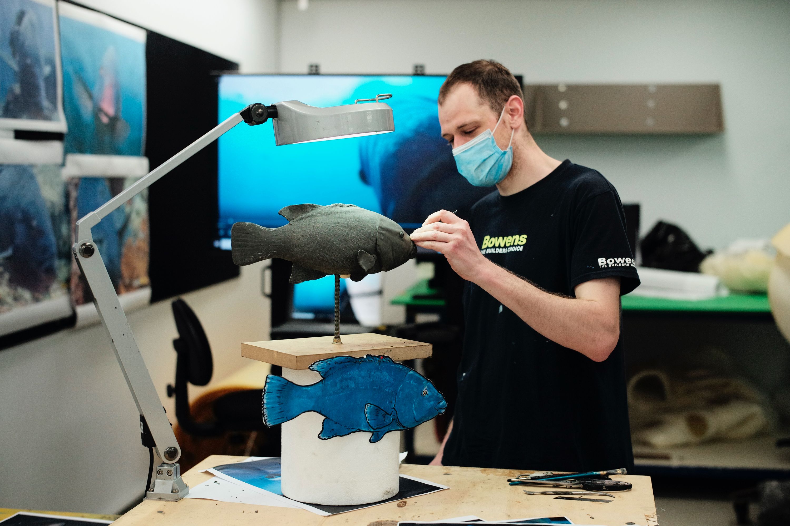 Photograph of a man working on a clay sculpture of a fish.