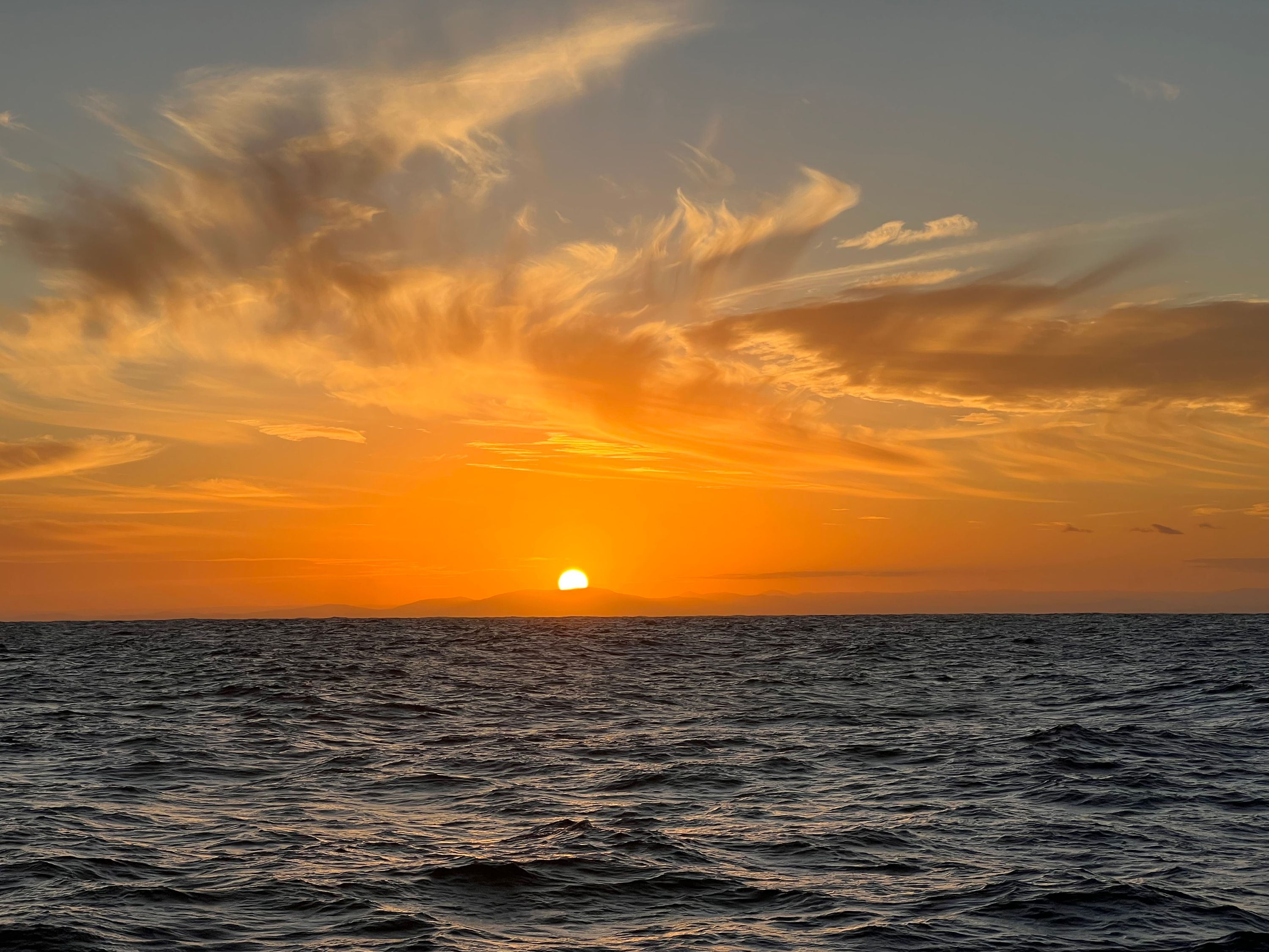 Photograph of ythe sun low on the horizon, the light clours coloured with golden light over the sea
