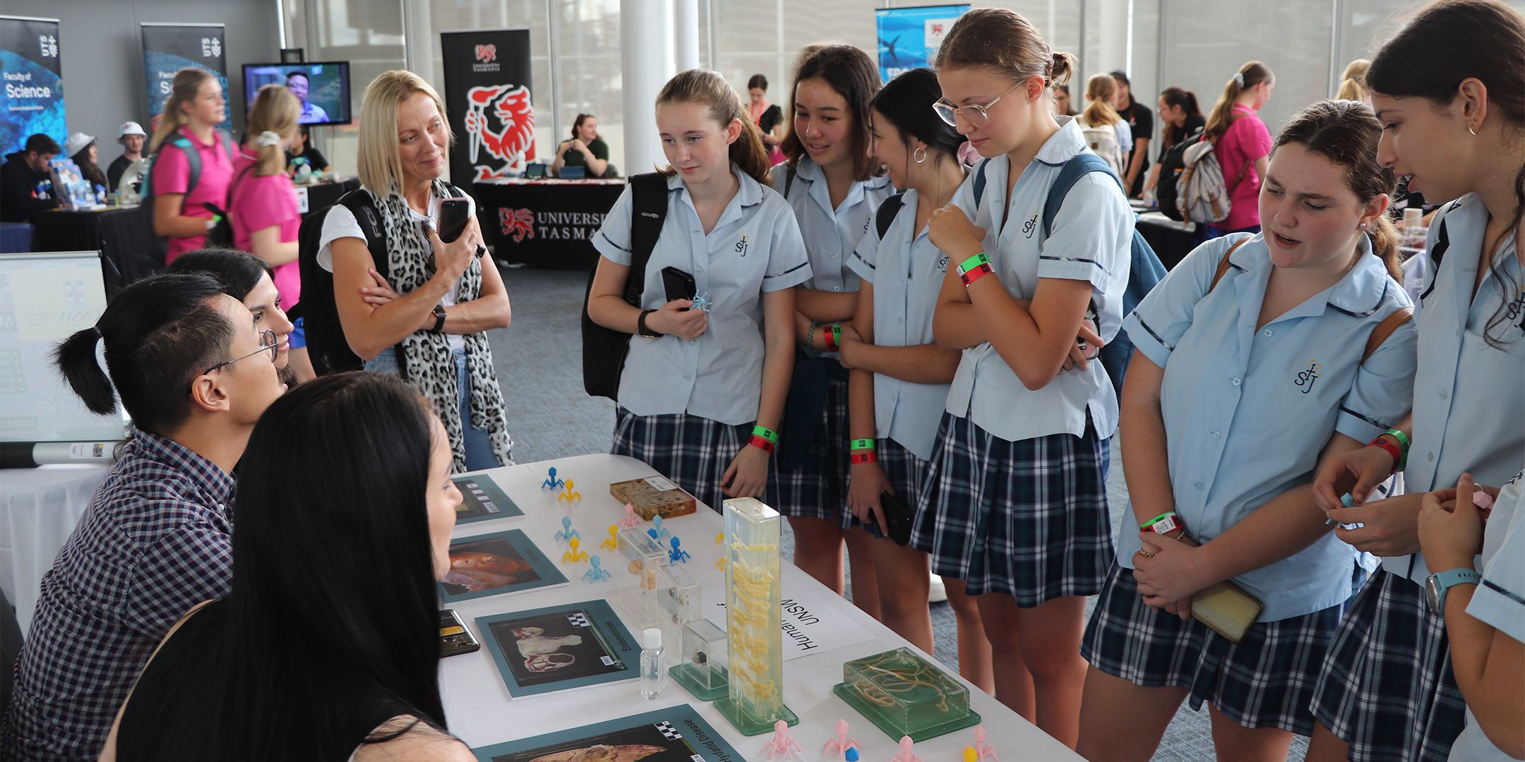 Photo of a large group of high school girls and their teacher talking to staff at a science expo table