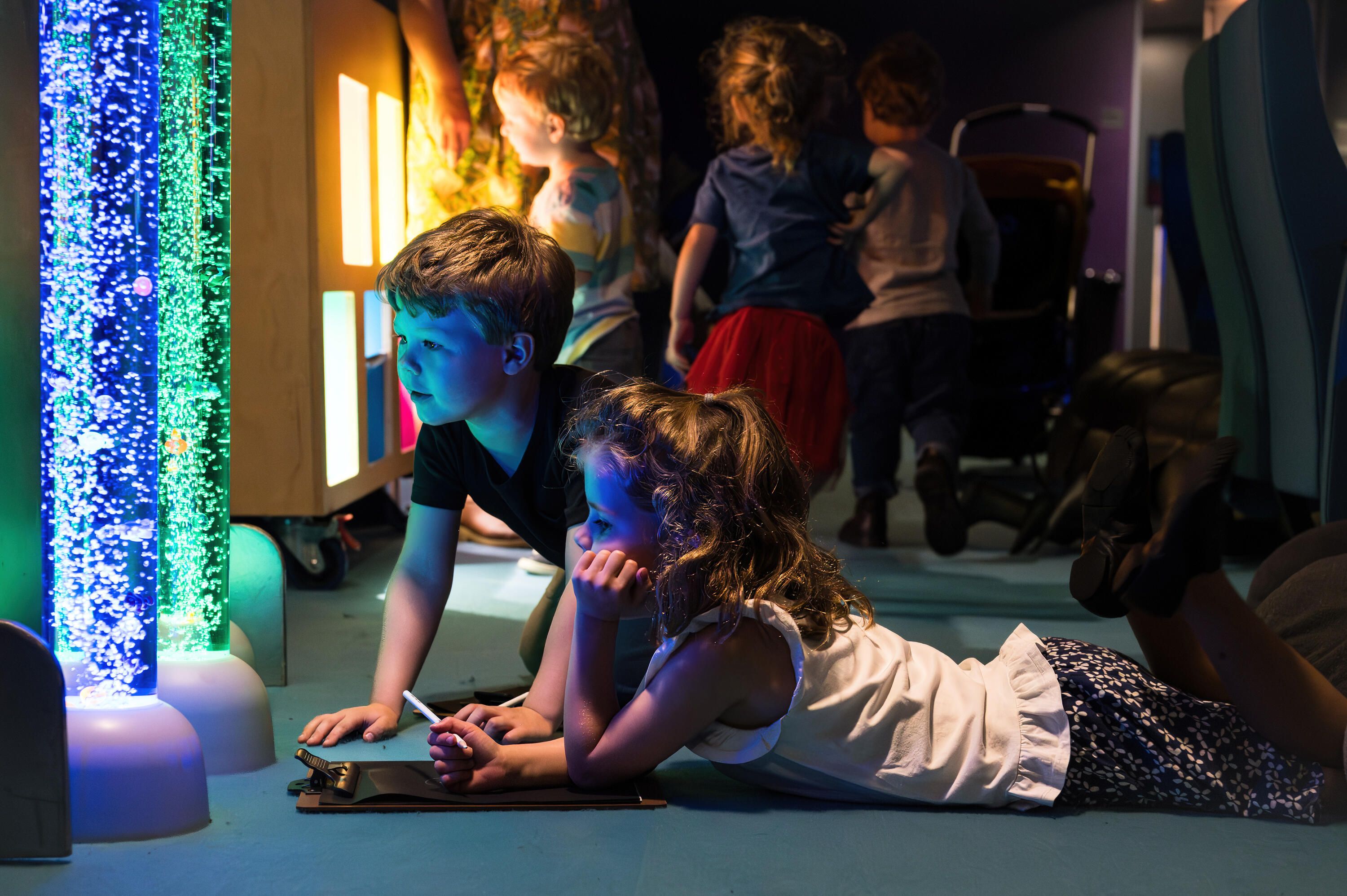 Photo showing children on the floor looking at tubes with coloured light and bubbles