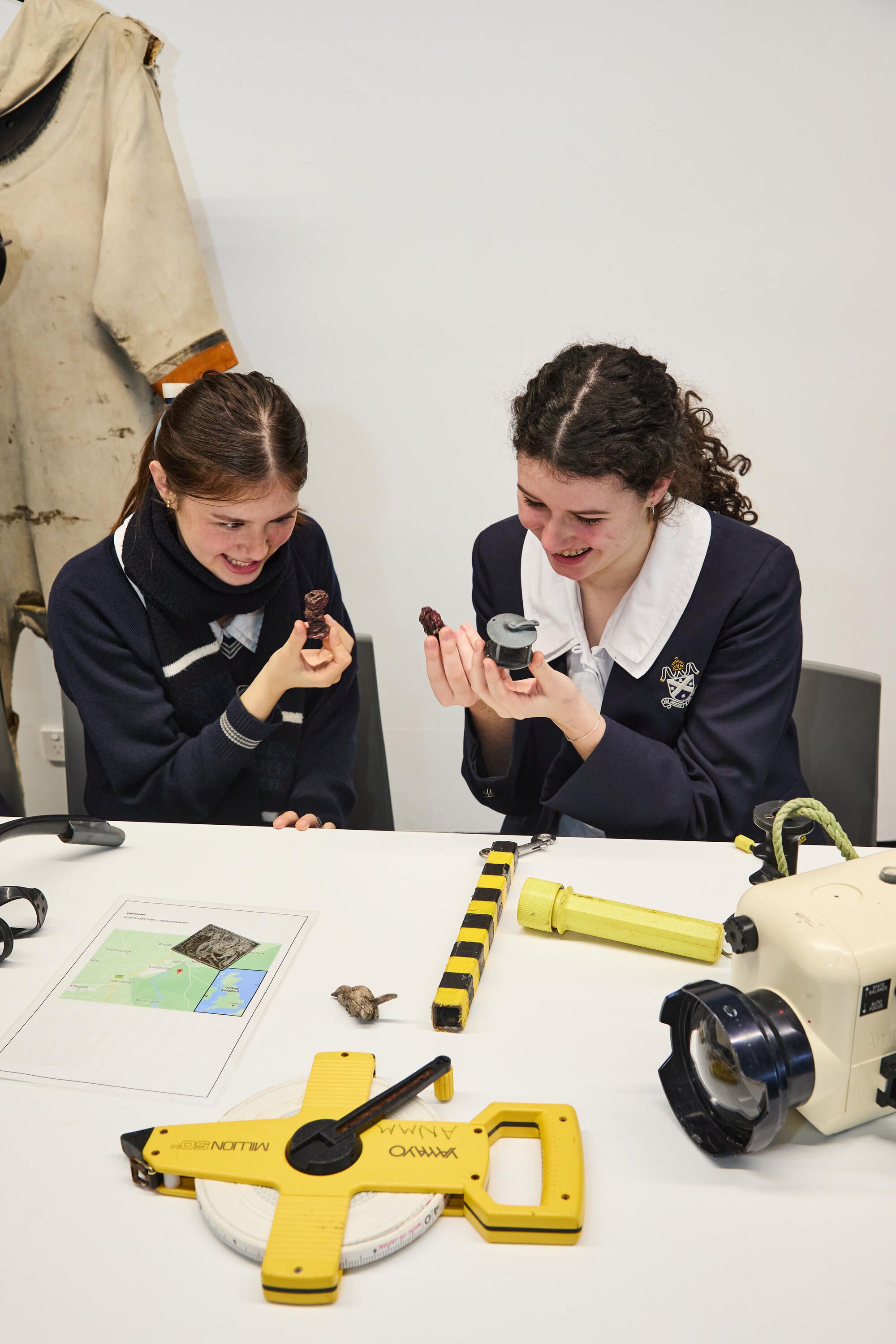 2 female students in navy school uniforms, looking down at artefacts