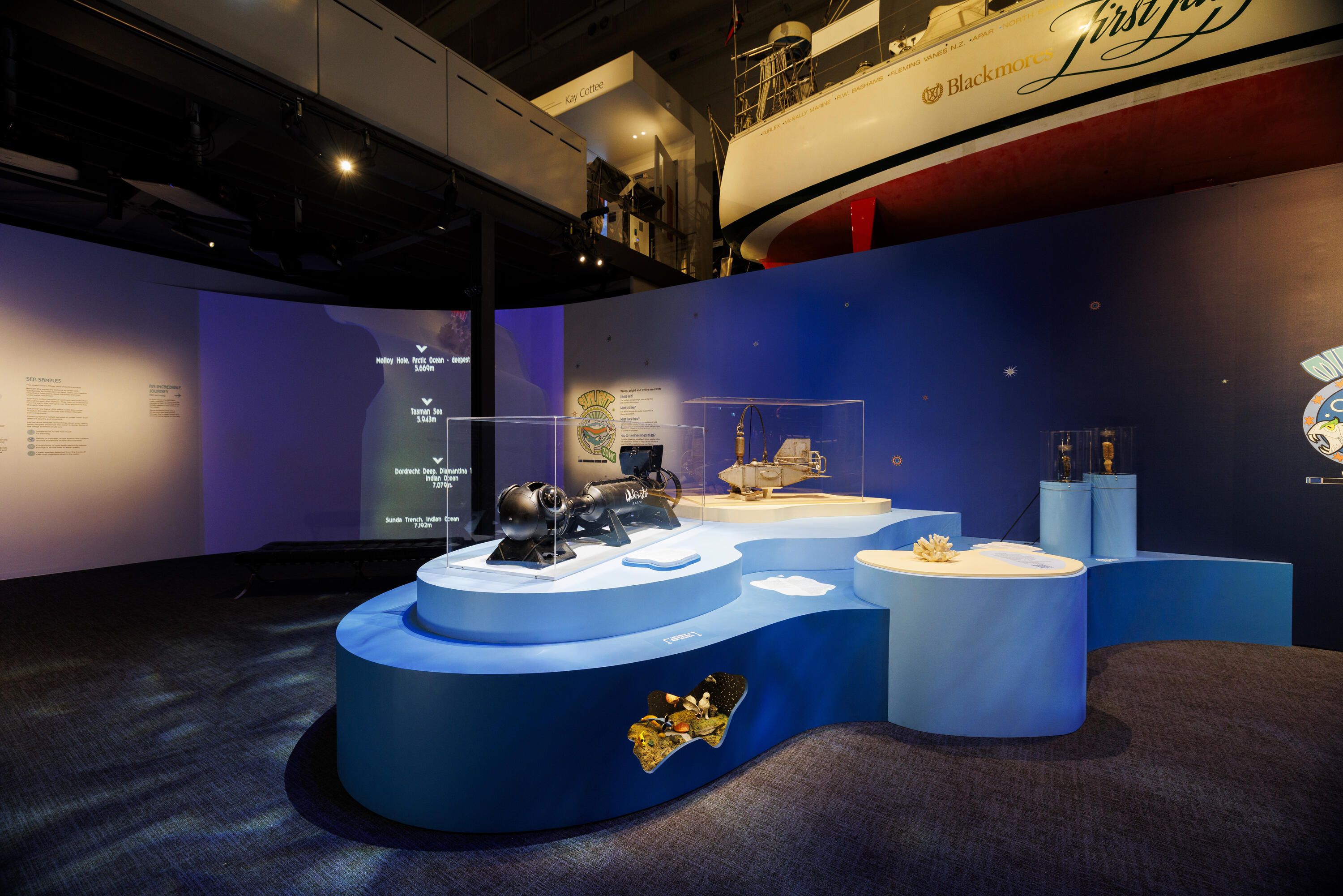 Photo of a blue curved plinth in a museum display with objects in clear perspex cases.