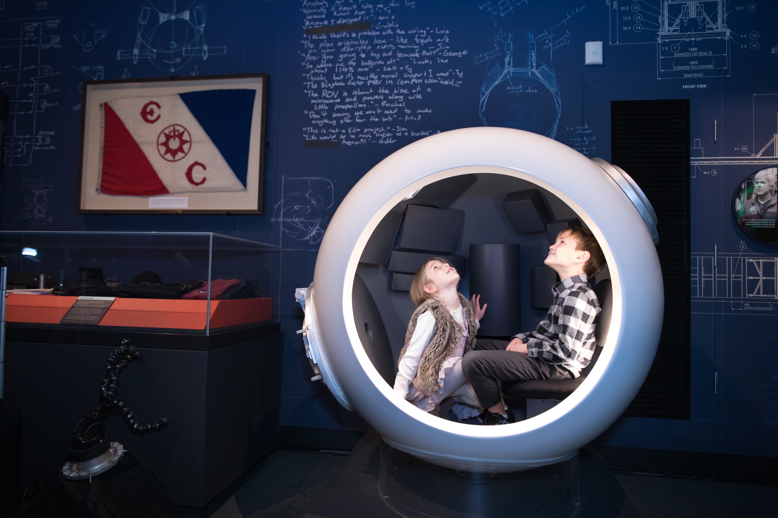 Photo taken inside an exhibition of two children in a round sphere looking up. 