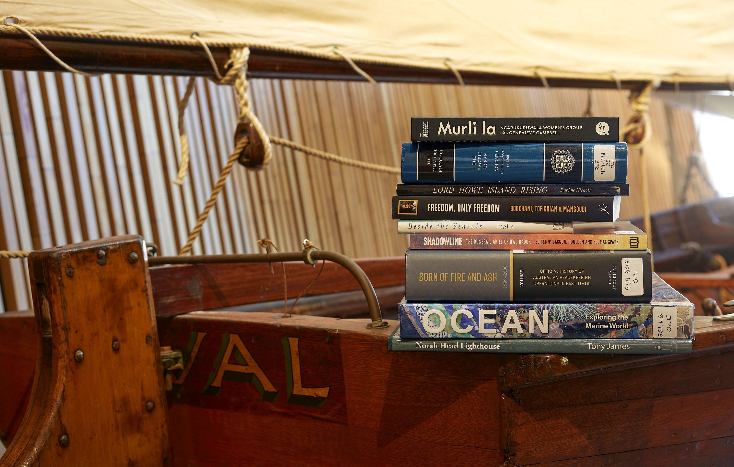 Pile of library books with different coloured covers sitting on the side of a wooden boat. 