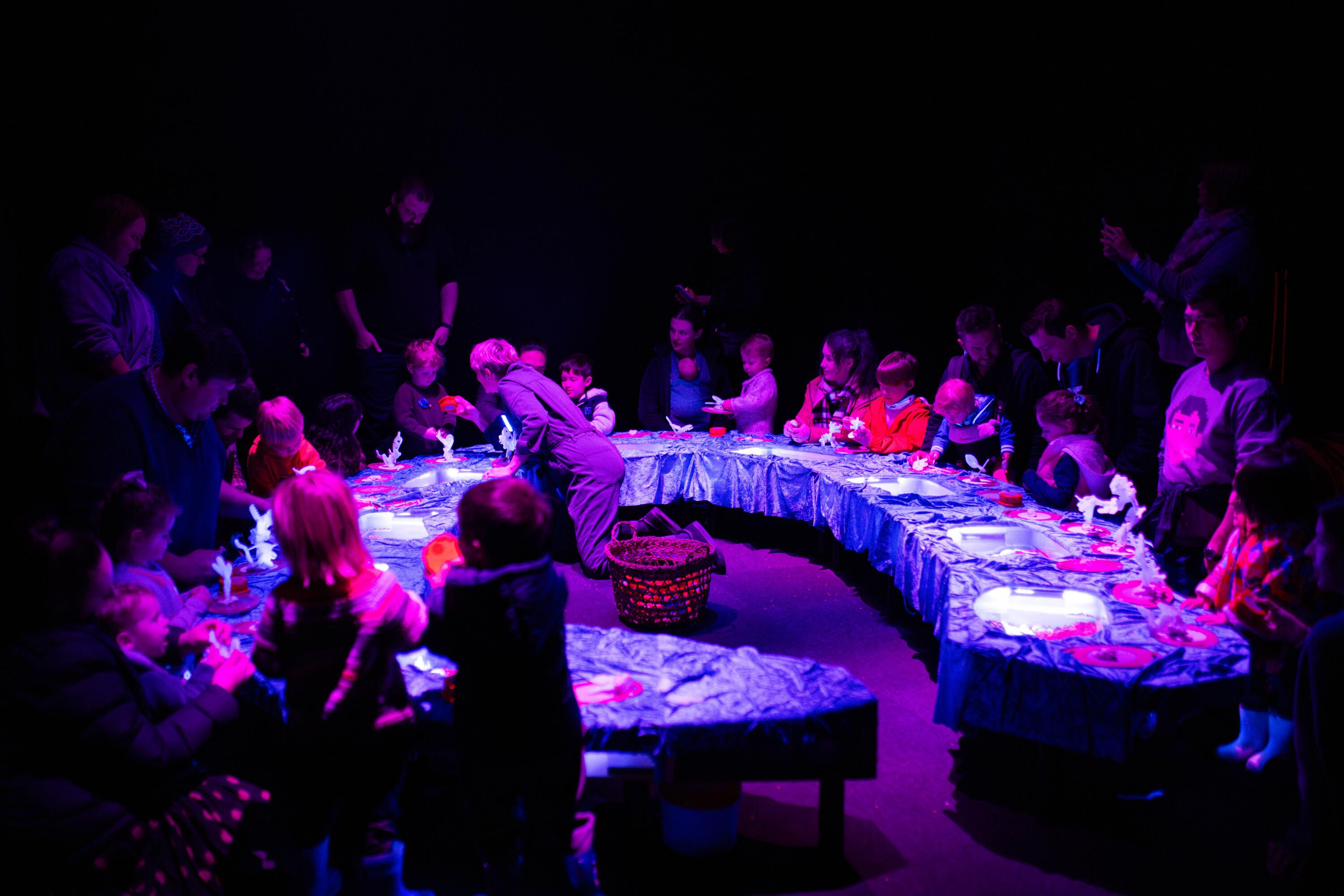 A round table with many people seated around it in neon lighting.