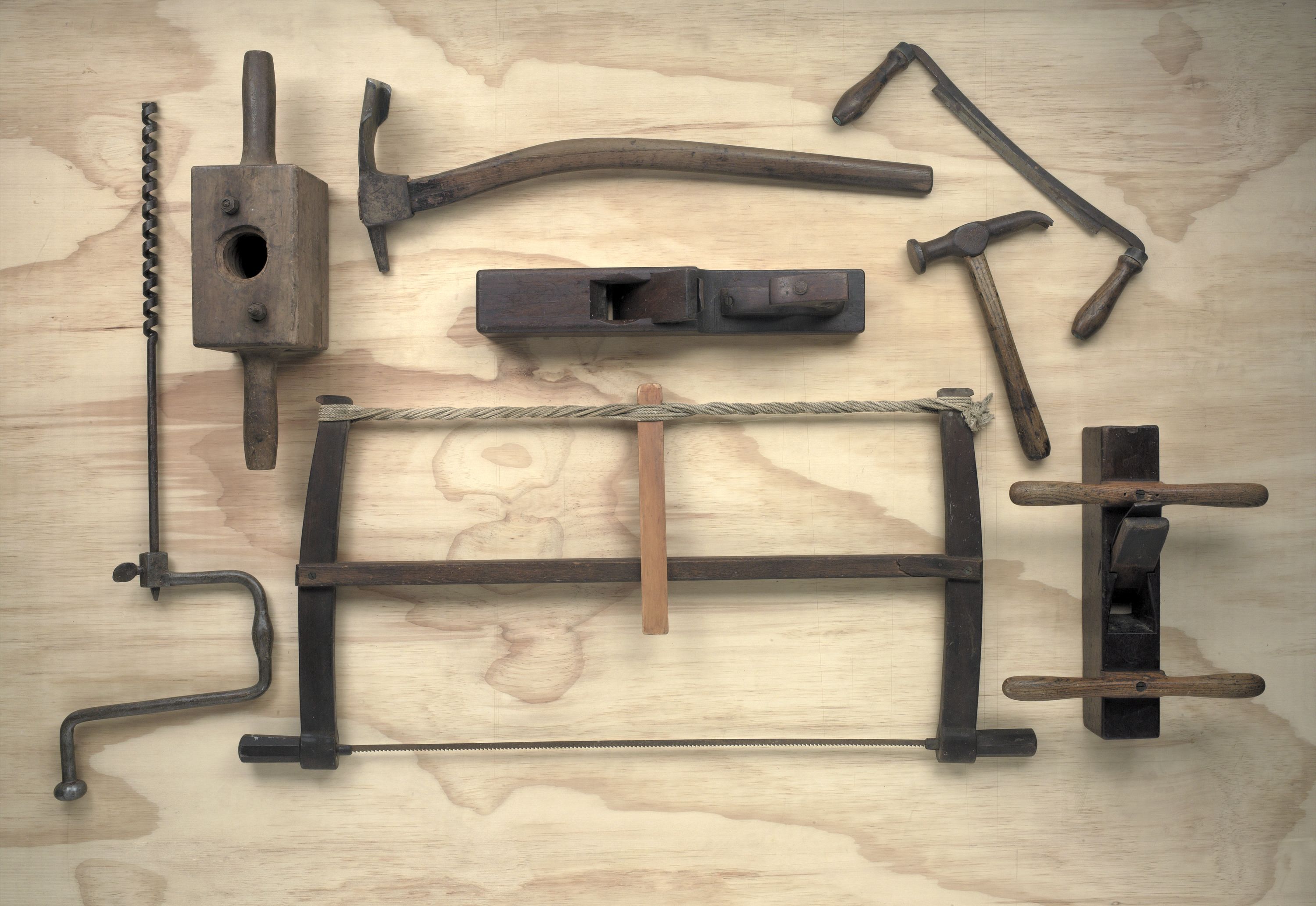 Photograph showing a selection of timber and metal boat building tools arranged on a wooden backdrop. 