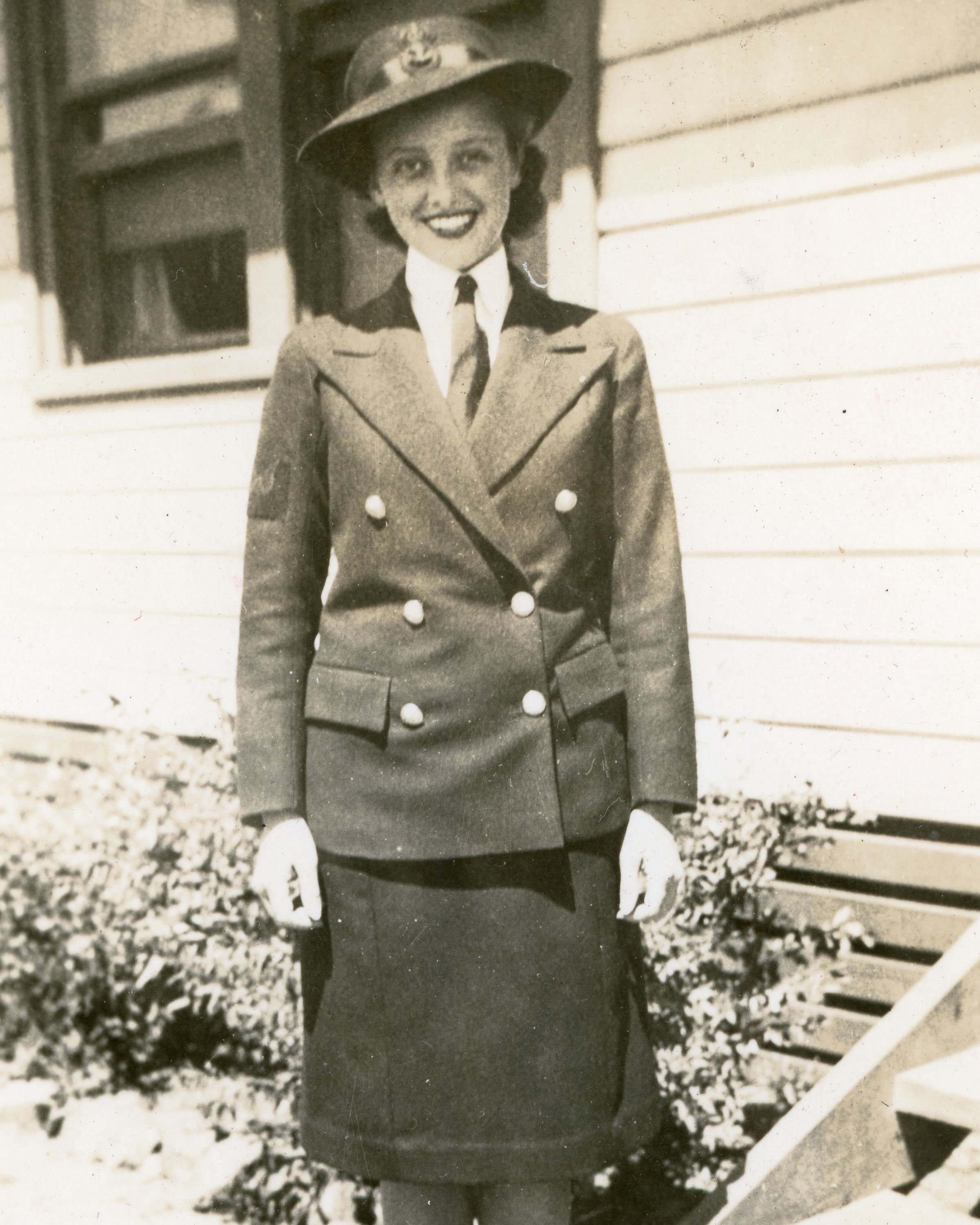 An old black and white photo showing a woman in a smart uniform and hat in front of a building