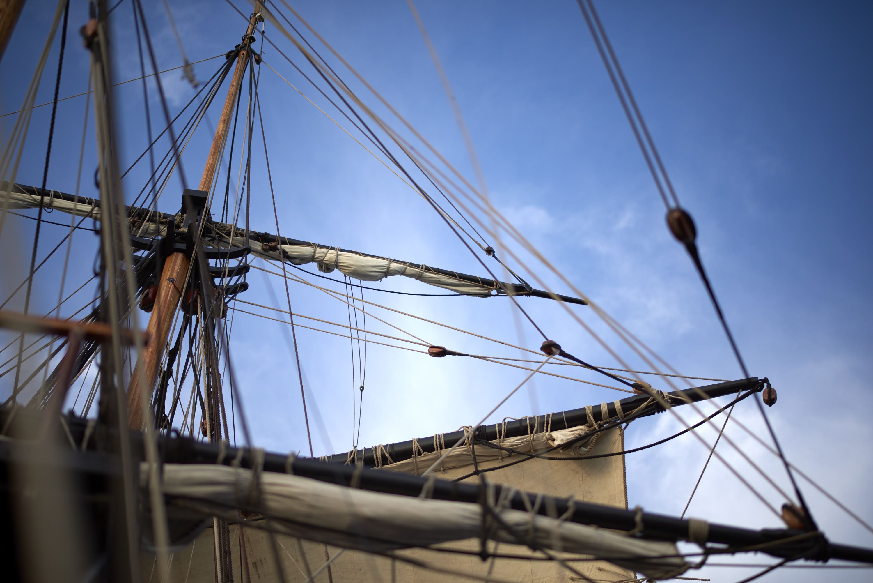 Photograph showing a tall ship masts, sails and rigging with a blue sky behind. 