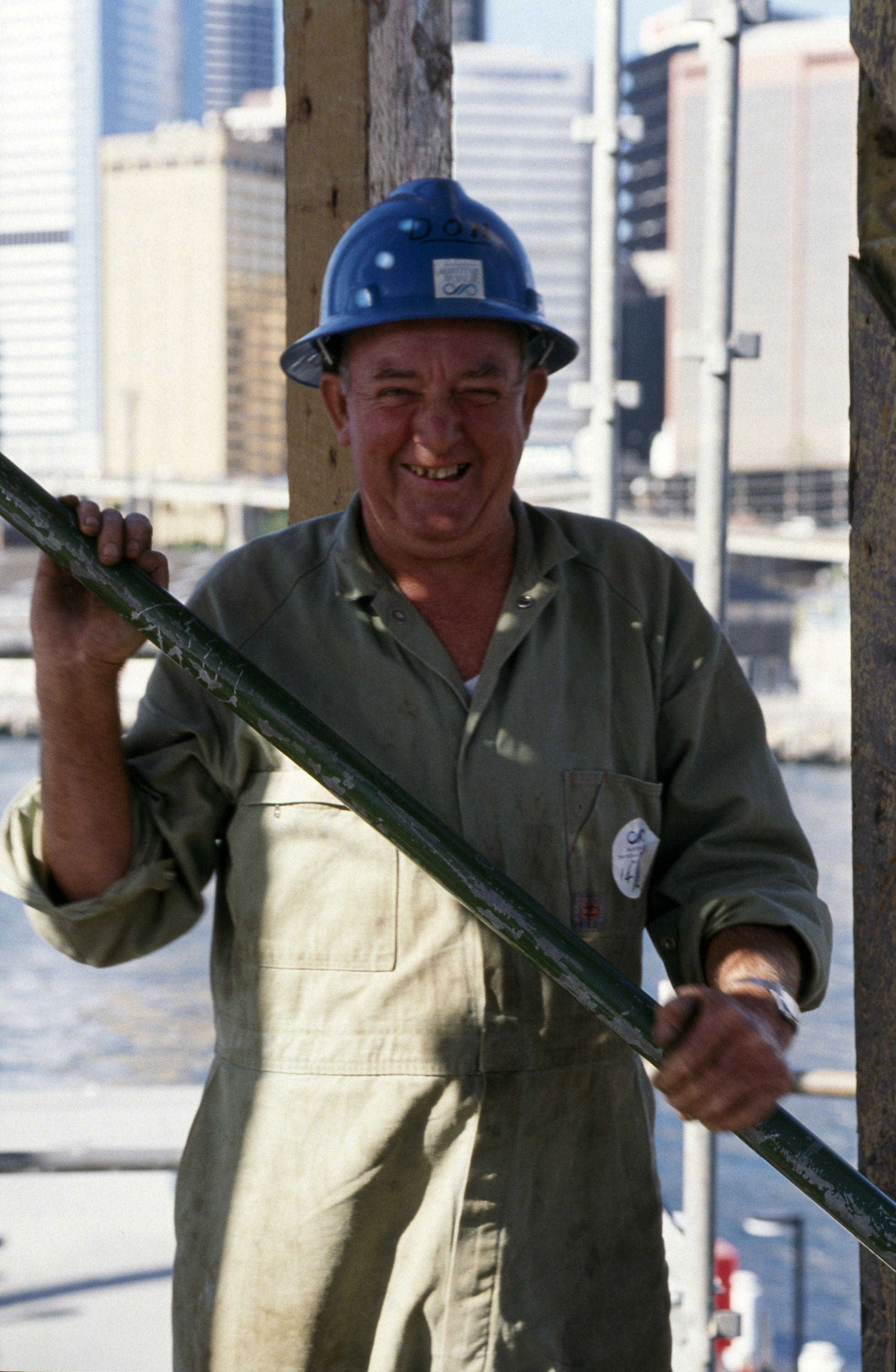 Photo portrait of a man wearing a hard hat and overalls, smiling towards the camera.