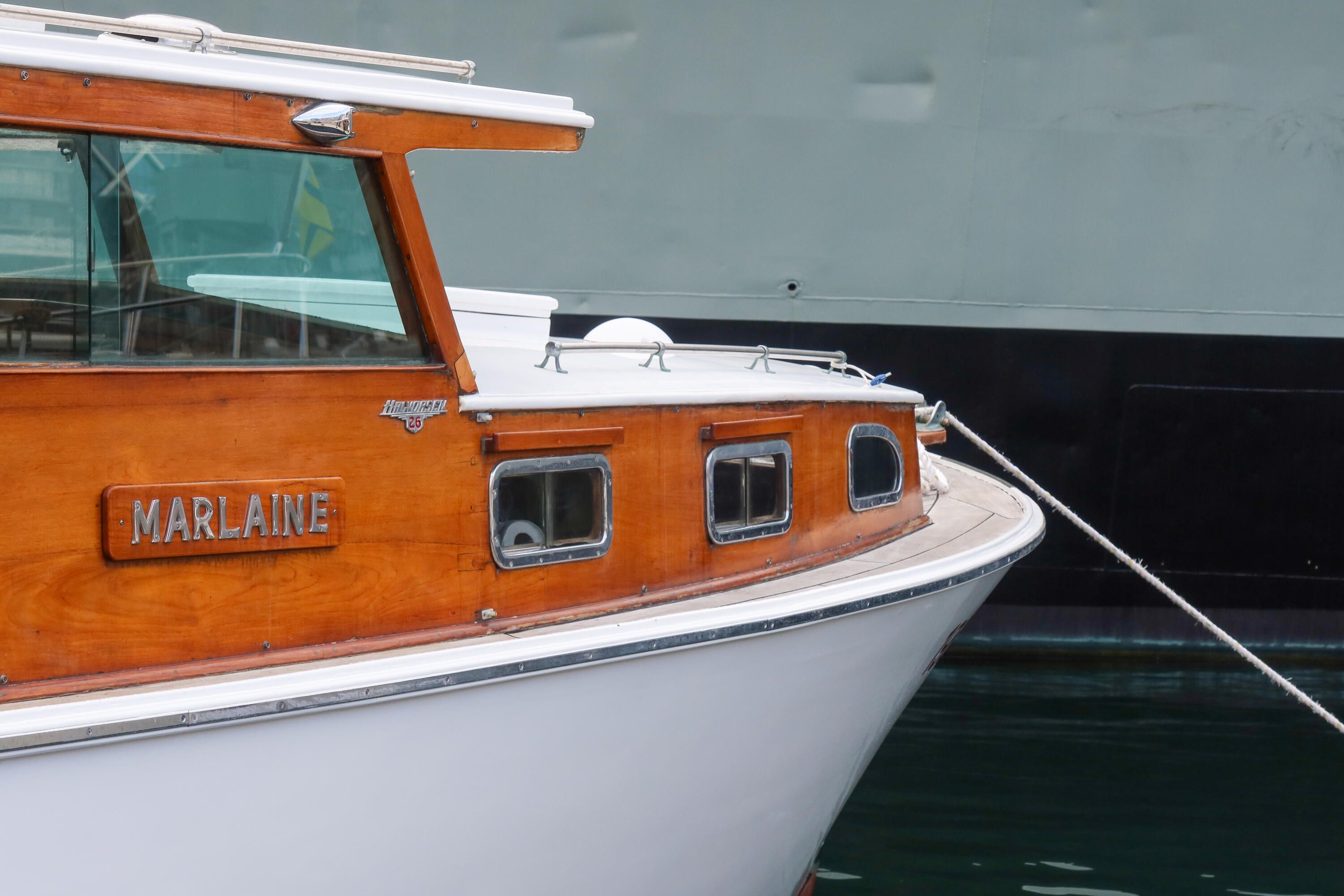 Close up photo of the front of a wooden boat, with a white hull and roof, and a nameplate which reads "Marlaine" 