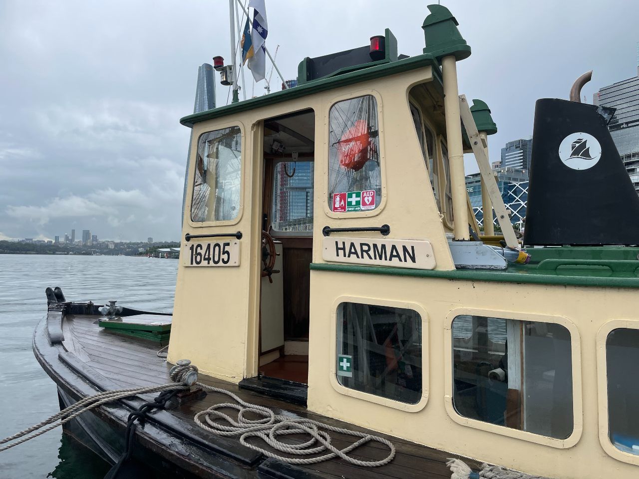 Close up photo of a light yellow boat with green trim, with a painted wooden plaque saying "HARMAN"