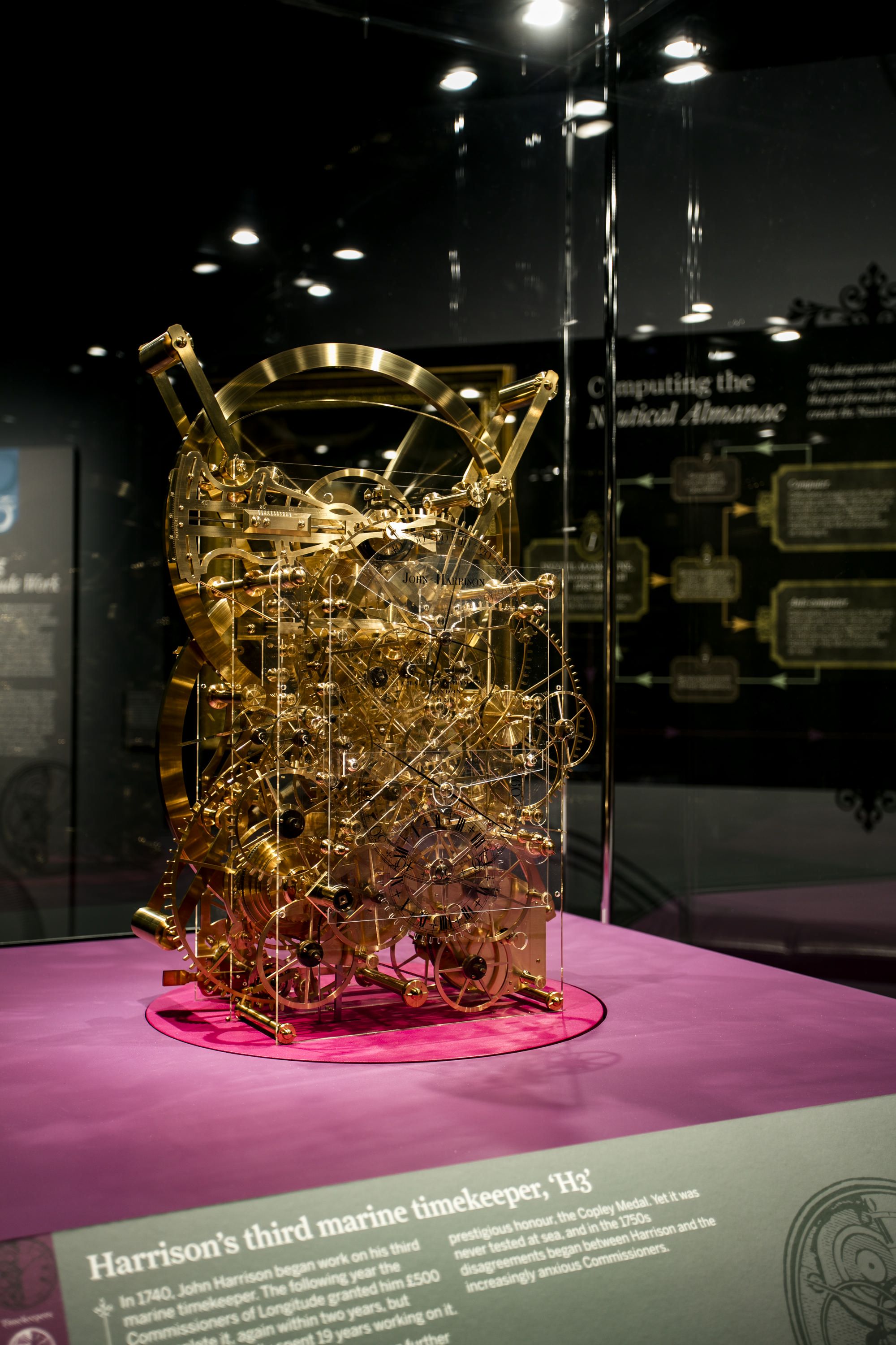 Photograph showing a gold coloured clock mechanism in a museum display case. 