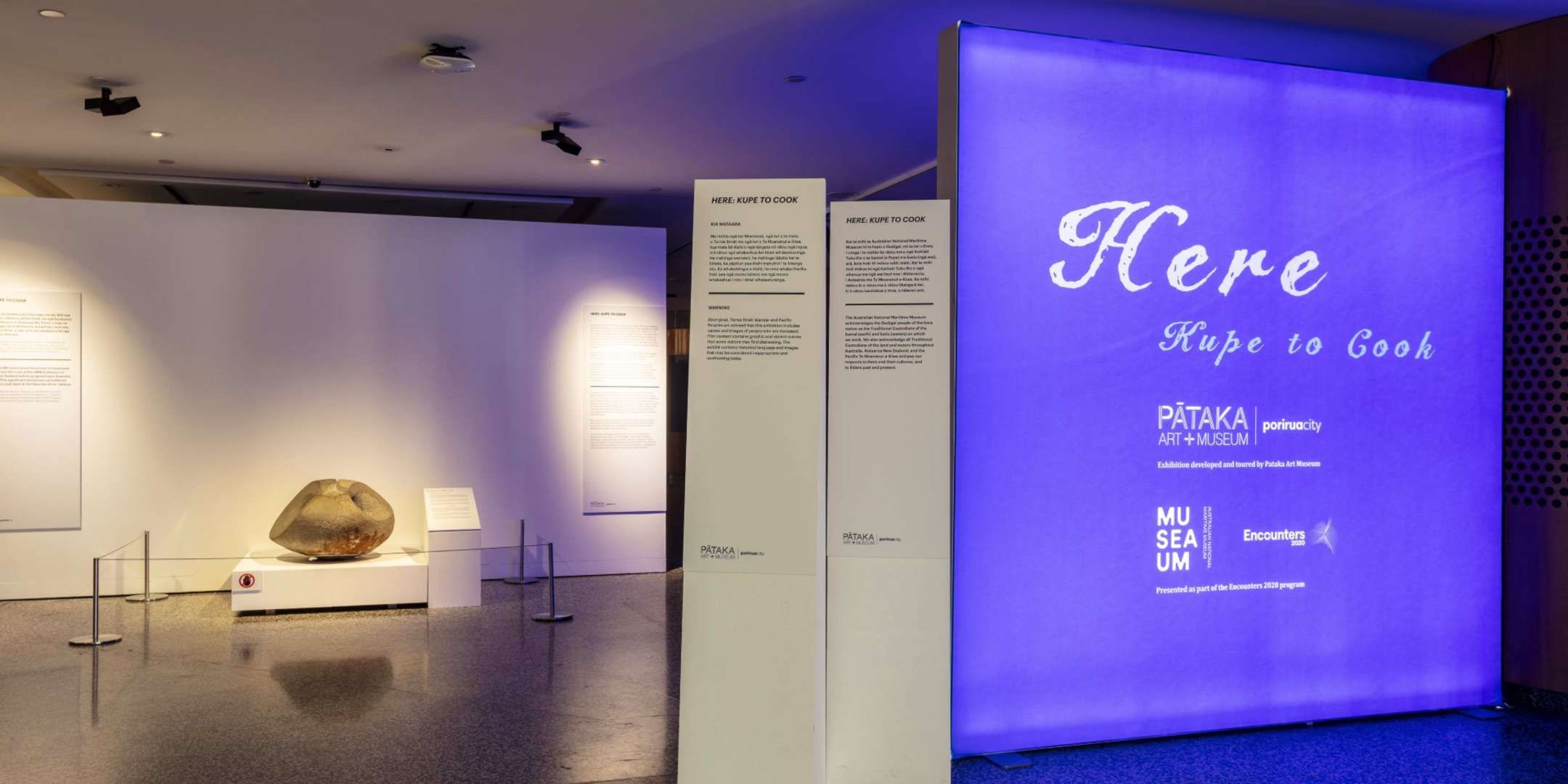 Photograph of an exhibition entry wall saying "Here: Kupe to Cook"