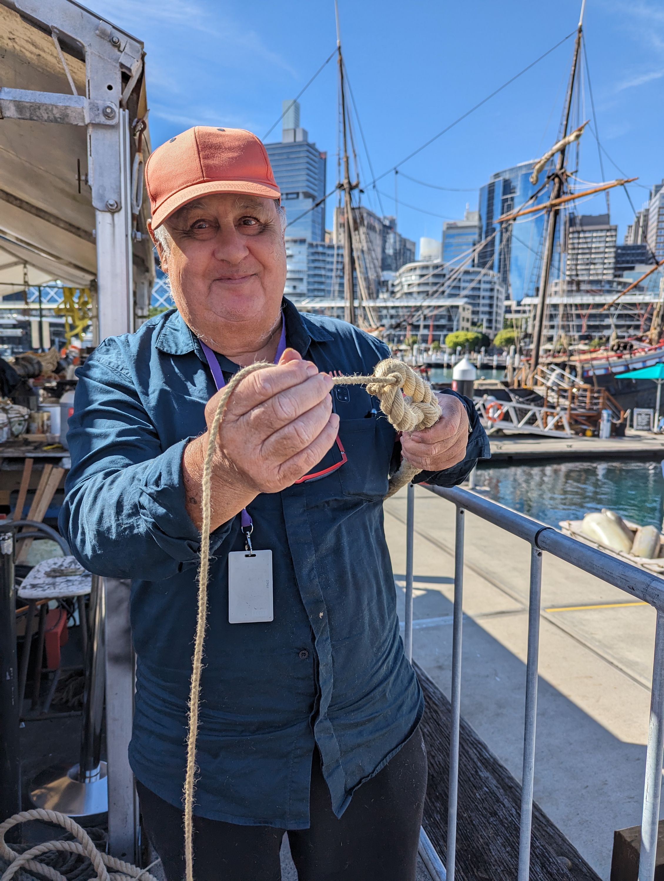 Photo of a man wearing an orange cap and blue uniform shirt, holding a knotted rope towards the camera.