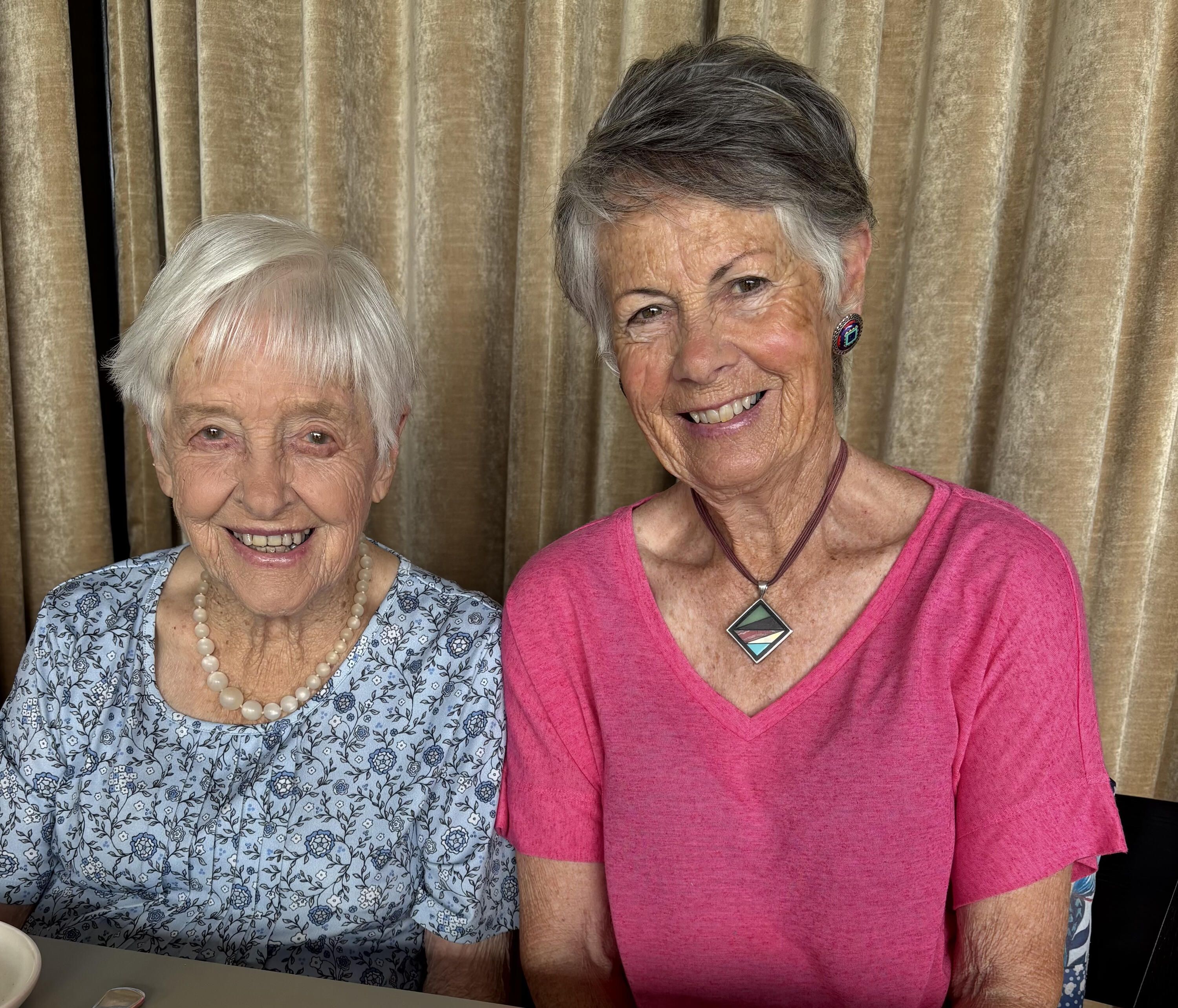 Photo of two women, on older with white hair wearing a blue patterned shirt, the other with grey hair and a pink shirt. 