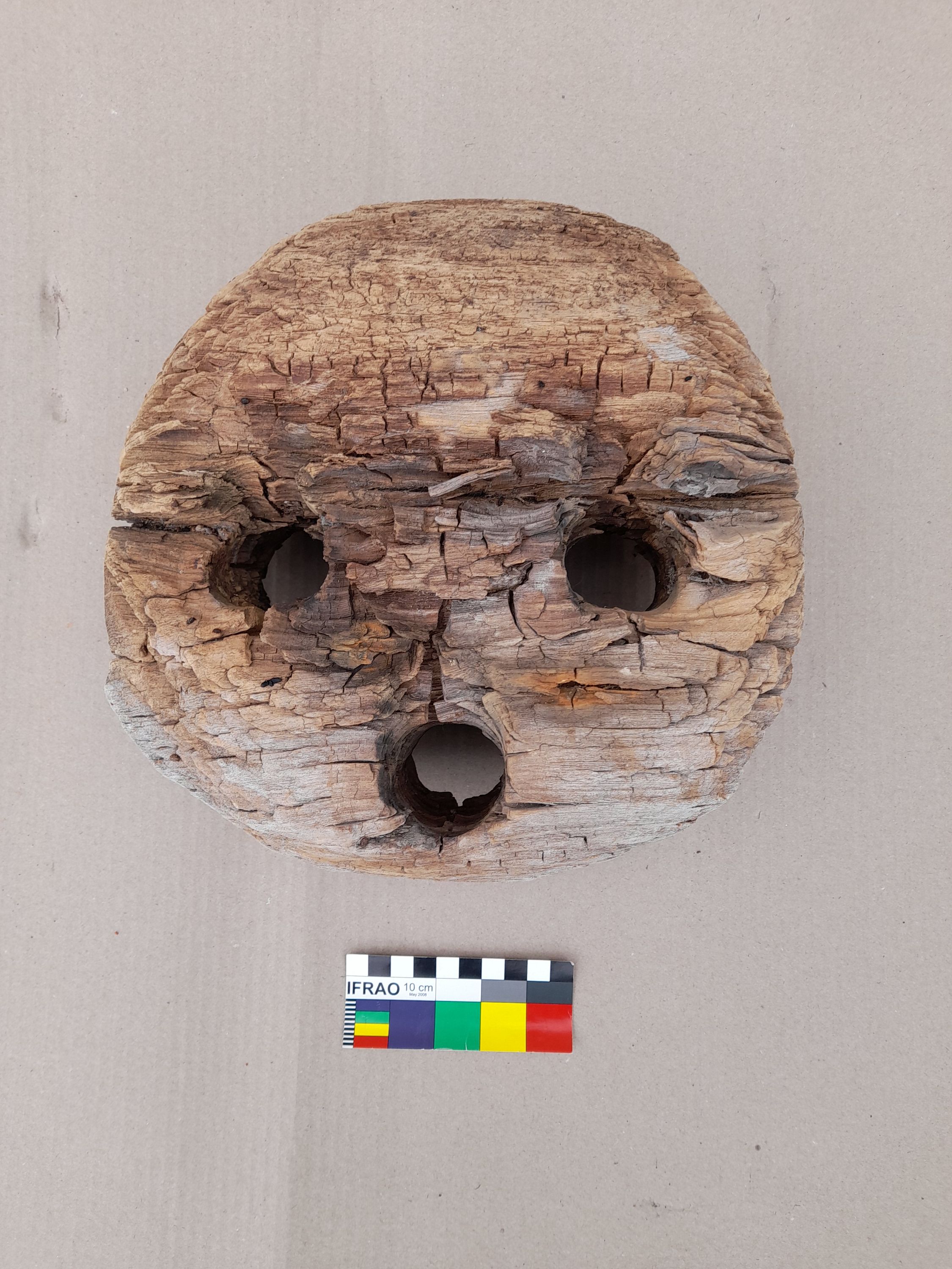 Photo of a worn, light coloured wooden object with 3 holes.