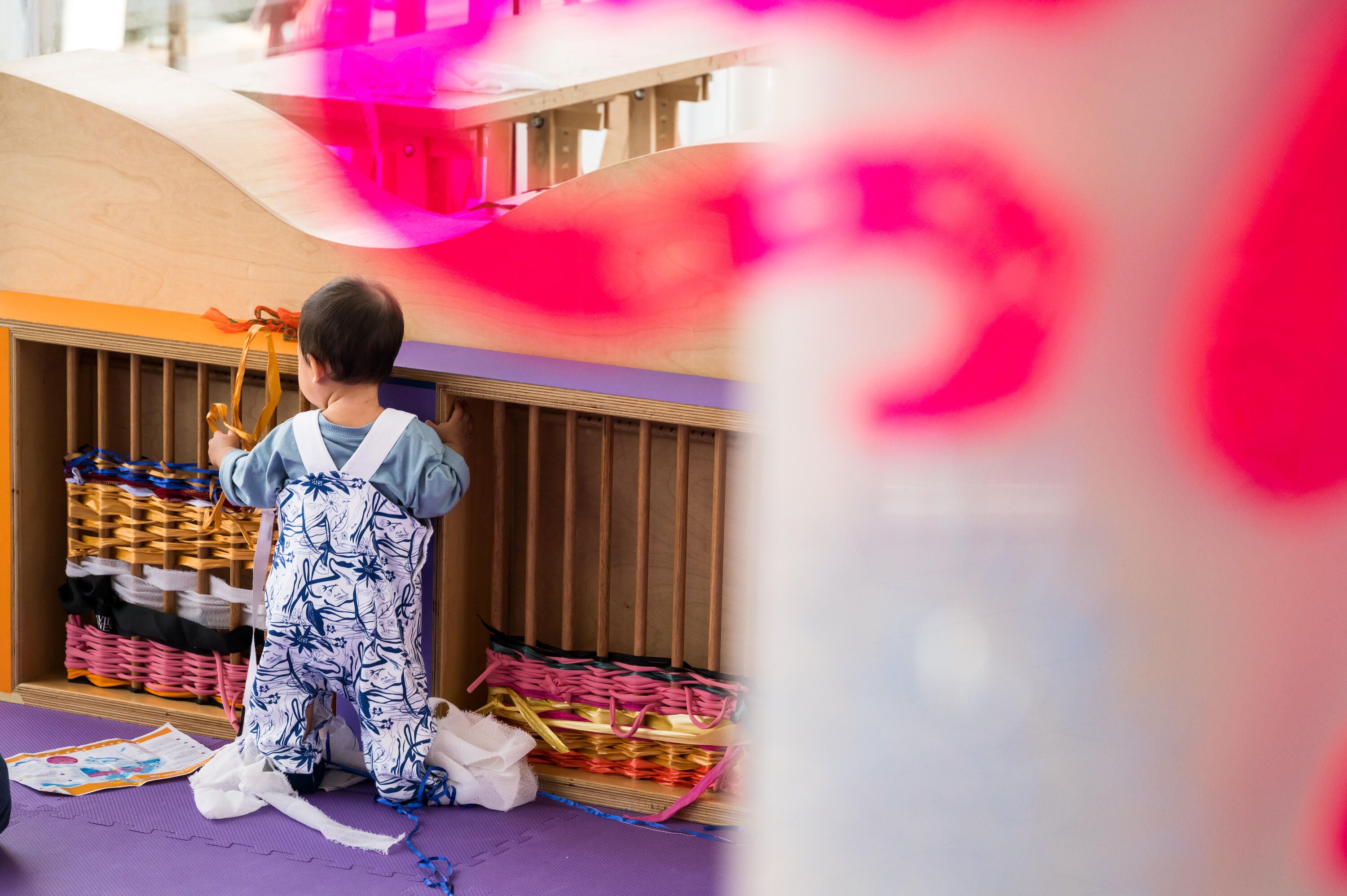 Photo of a young toddler holding on to a weaving activity in a kids activity space