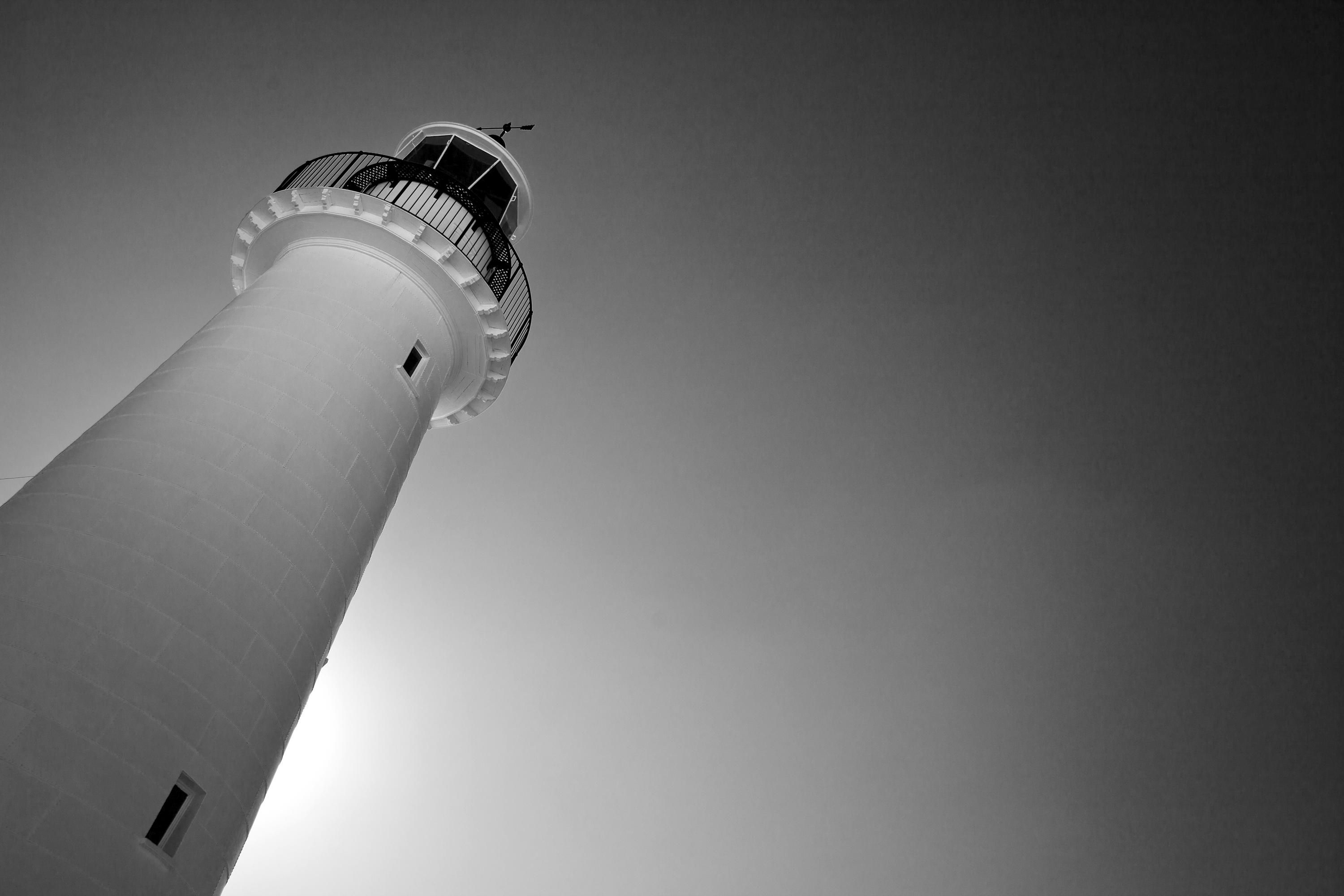 Black and white photo showing the museum lighthouse shot from below at an angle lit by the sun from behind.