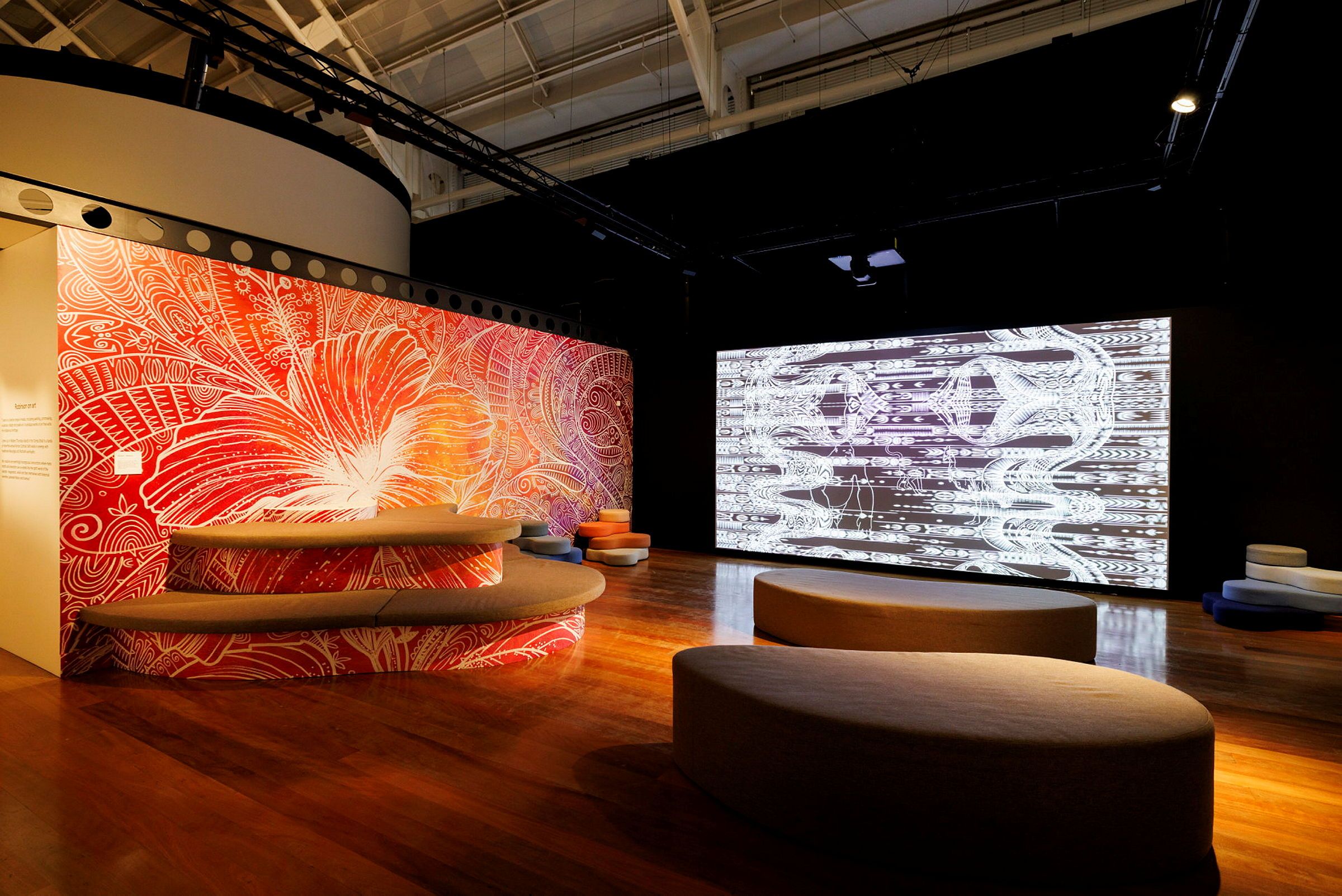 Photo of a museum exhibition display with a large screen and a colourful mural.