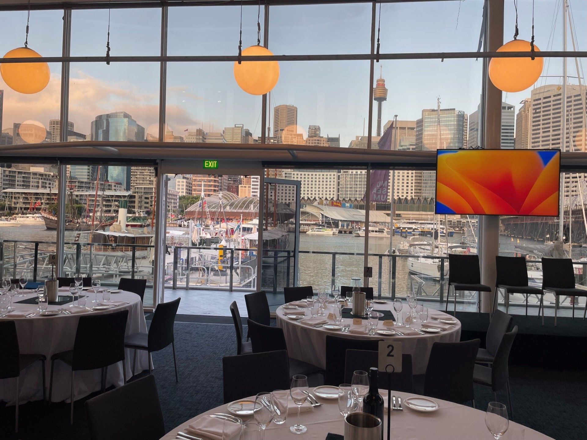 Photo of a museum event space with round tables. The Darling harbour waterfront is in the background. 