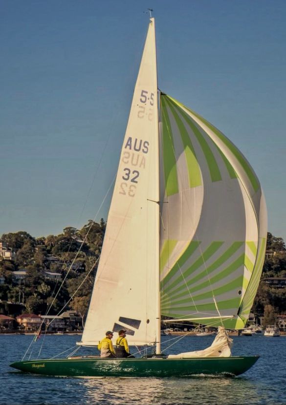 Photo of a sailing boat, the left triangular sail is white, and the other is white with a green stripped pattern