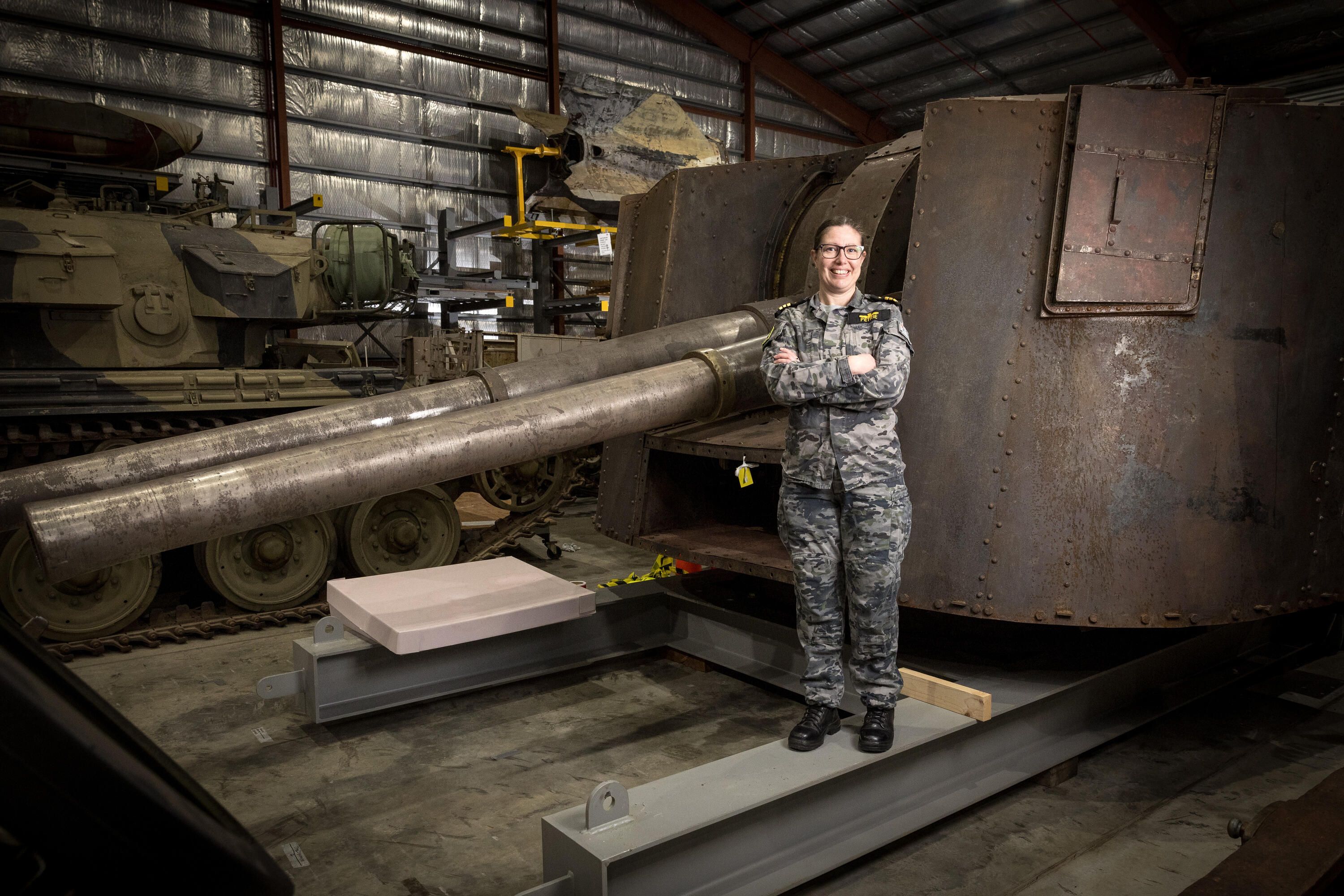 Photo of a woman in a camouflage pattern military unifom standing on a brown tank.